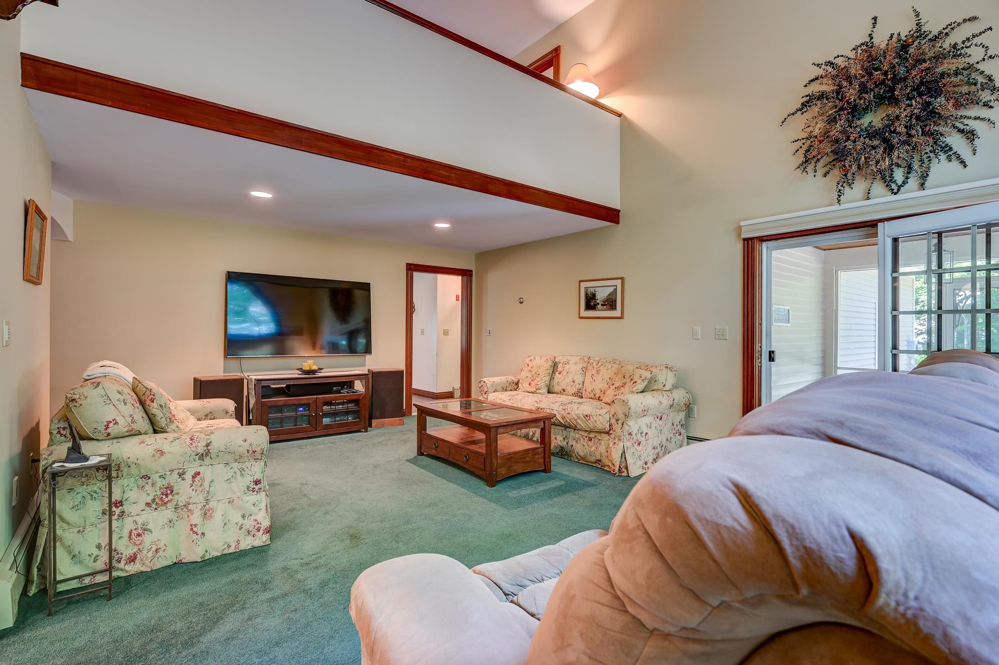 Furnished living room with floral sofas, a loft railing, and a sliding glass door.
