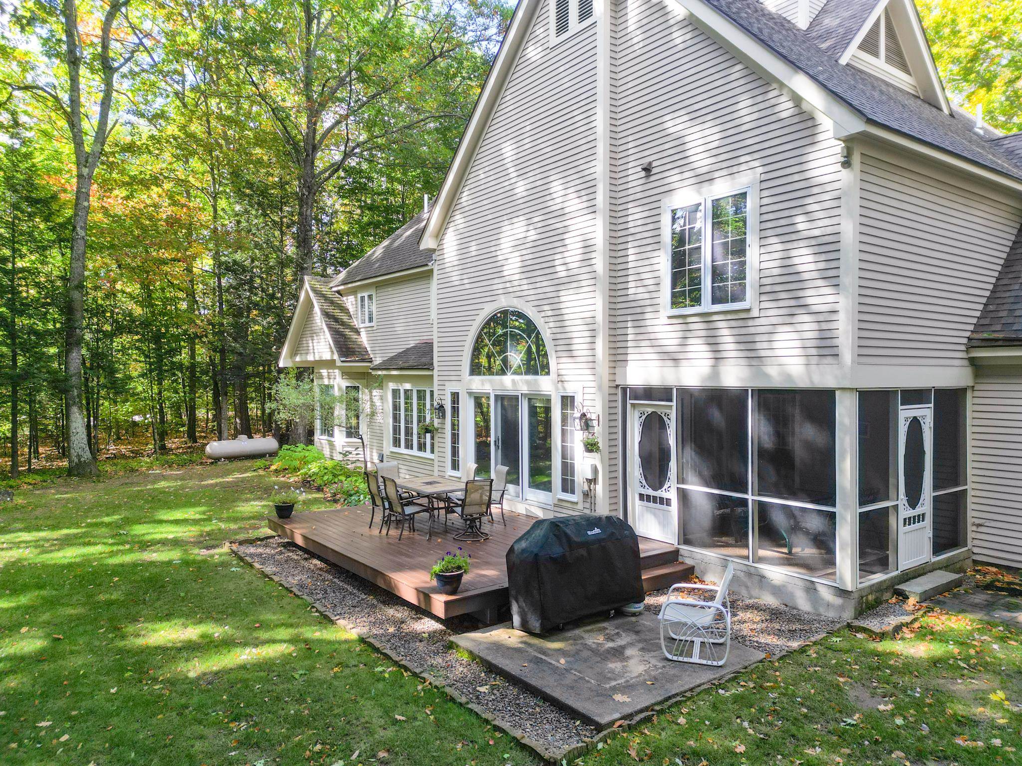 House exterior with a screened porch, raised deck, and wooded backyard.