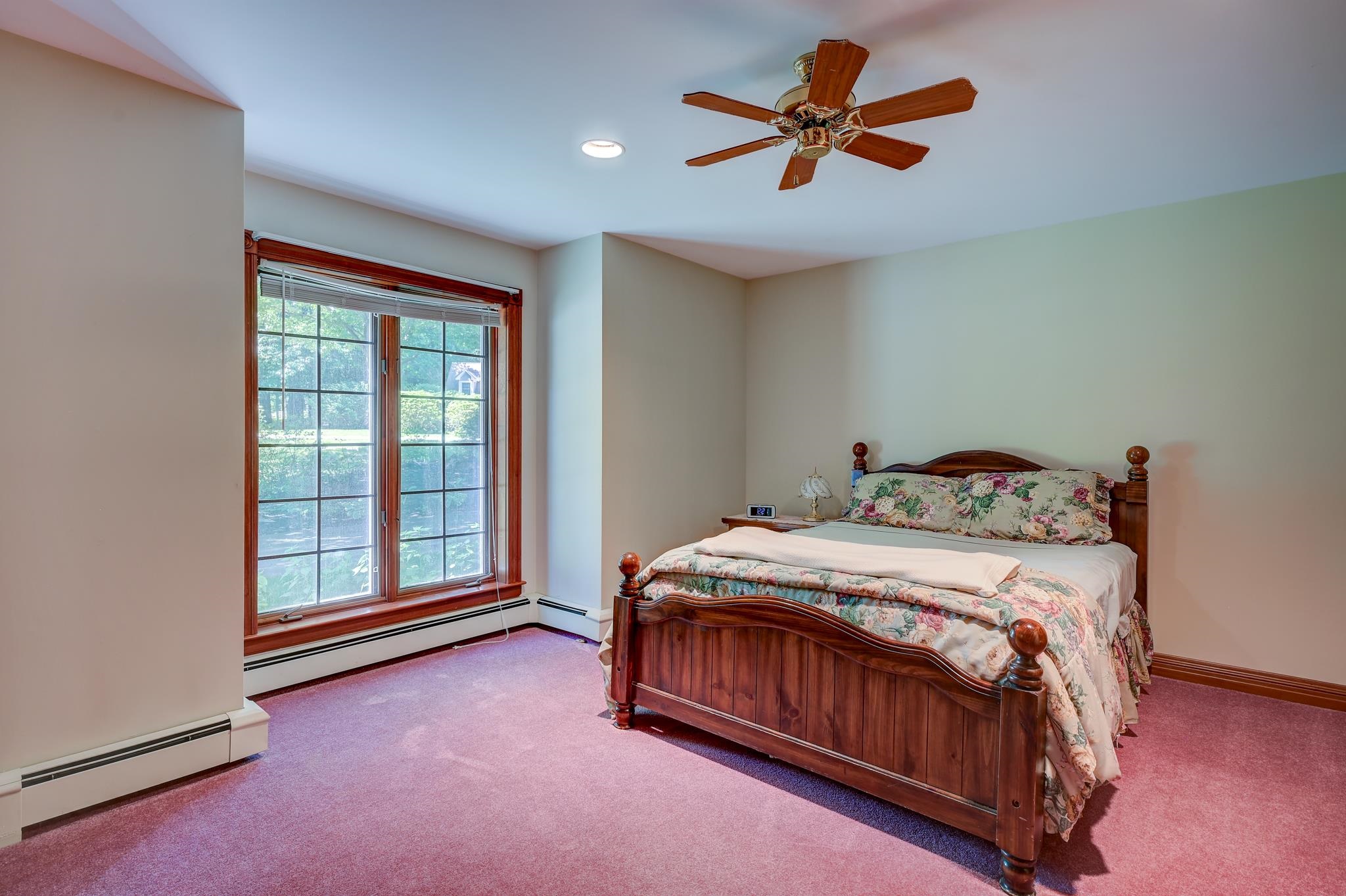 Bedroom with a wooden bed, floral bedding, and a large window overlooking greenery.