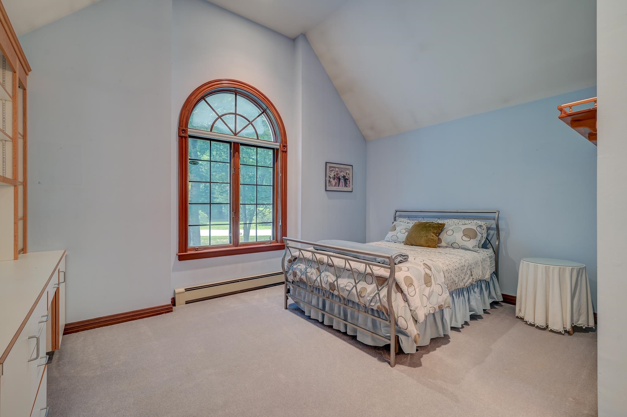 Bedroom with a high vaulted ceiling, an arched wood-trimmed window, and a metal-framed bed.