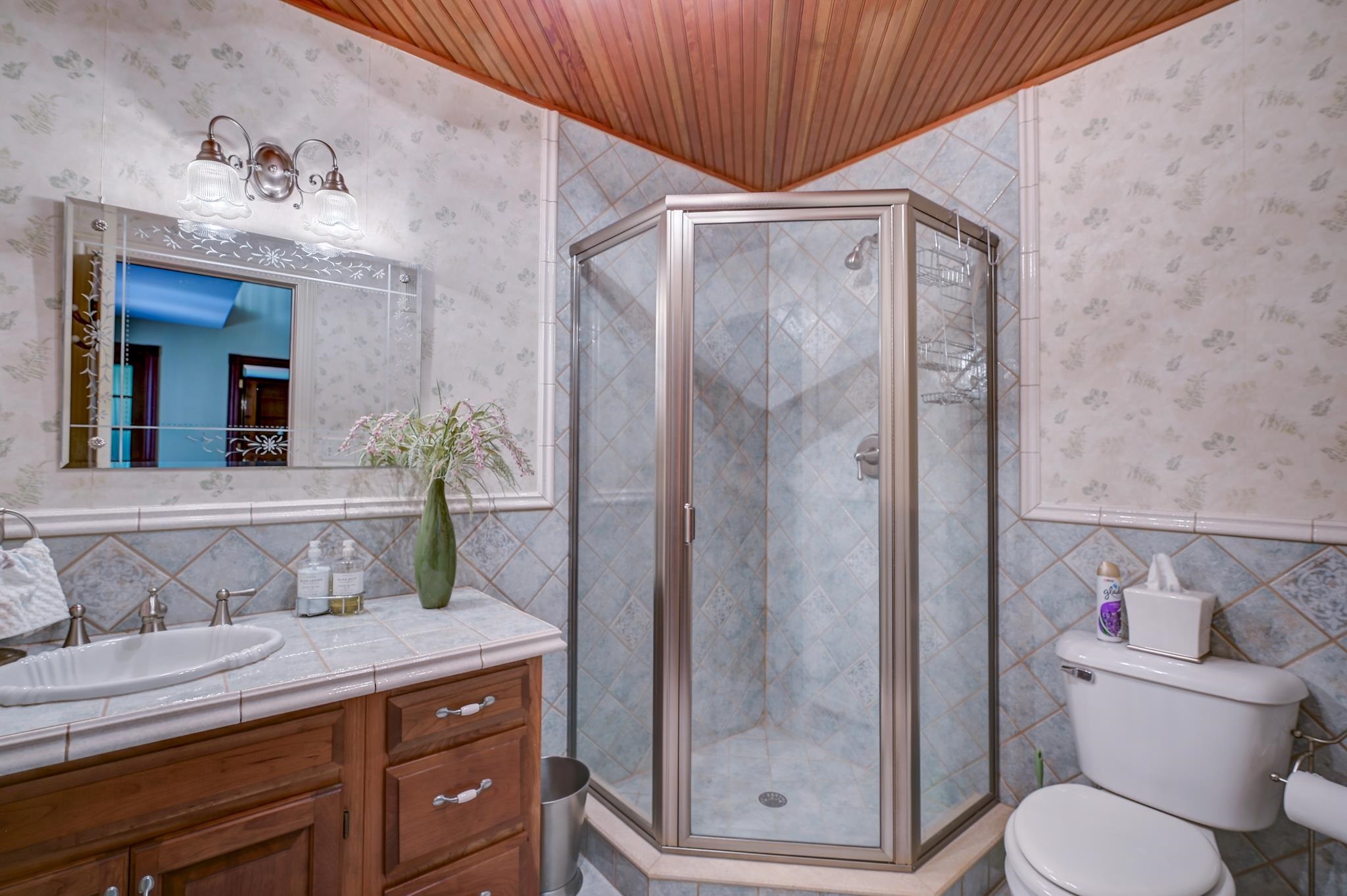 Bathroom with a glass corner shower, tiled vanity, and wood-paneled ceiling.