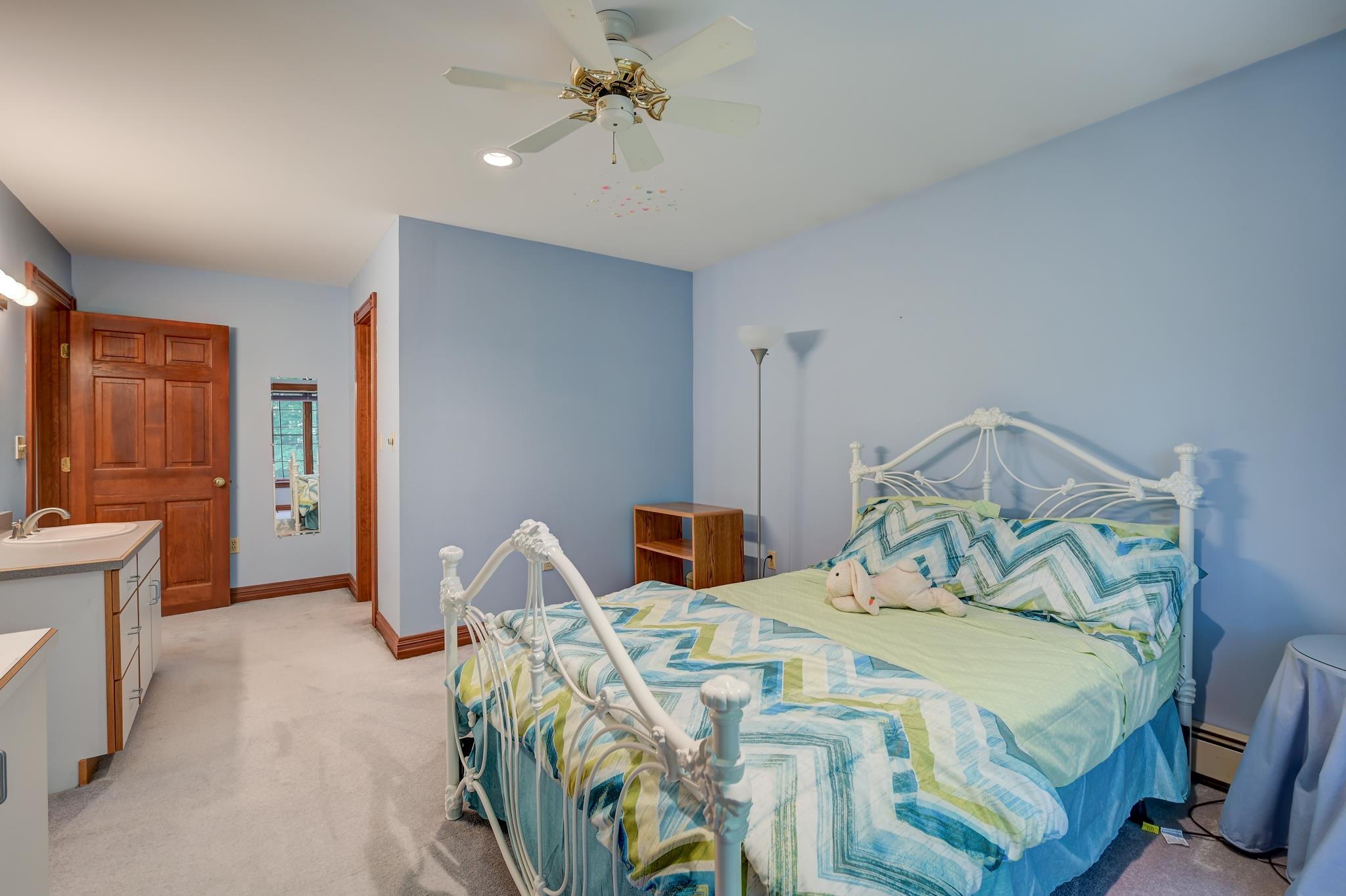 Bedroom with a white iron bed, blue walls, and colorful geometric bedding.