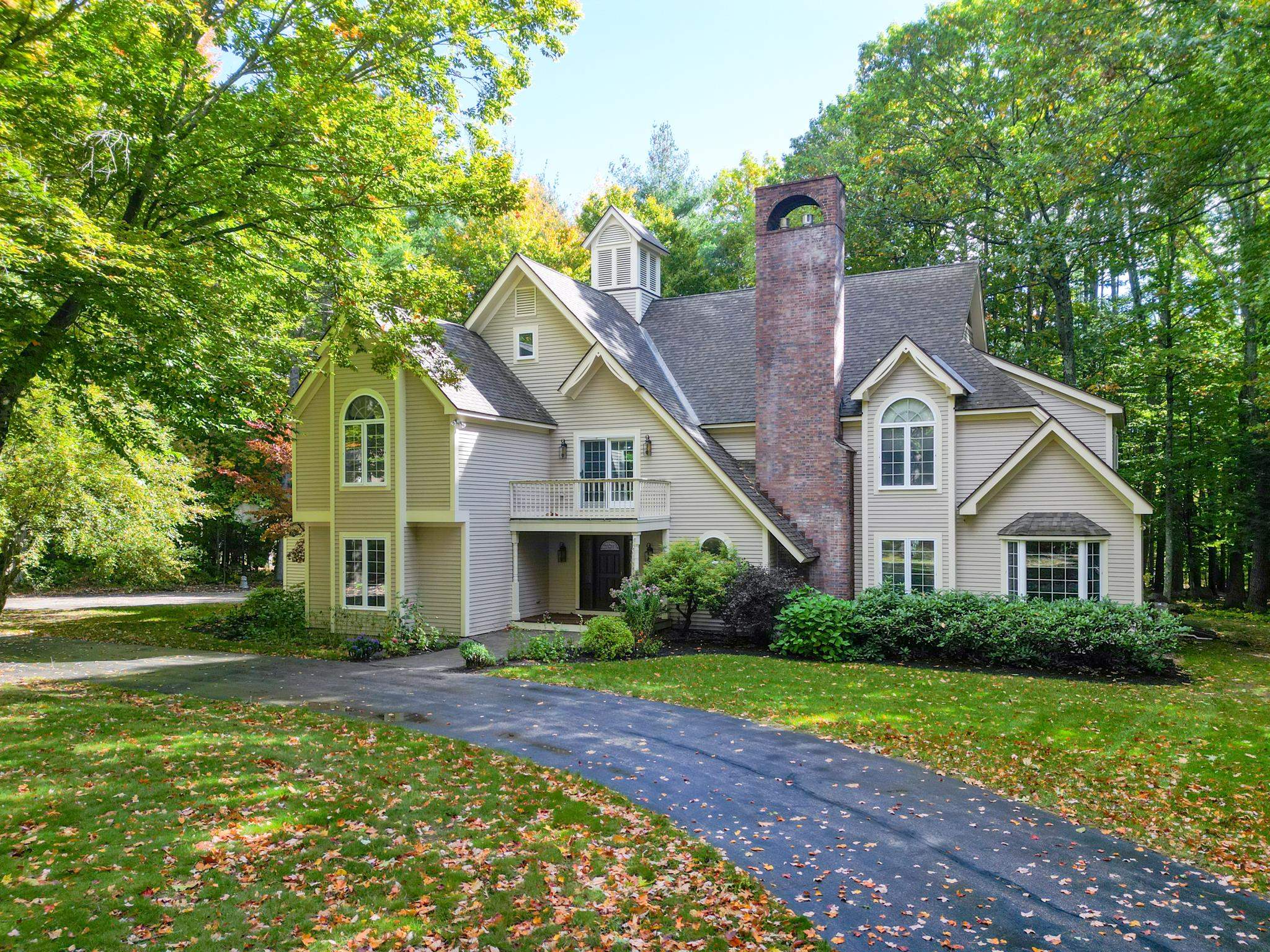 Large multi-gabled house with a tall brick chimney, surrounded by trees and a leaf-strewn lawn.