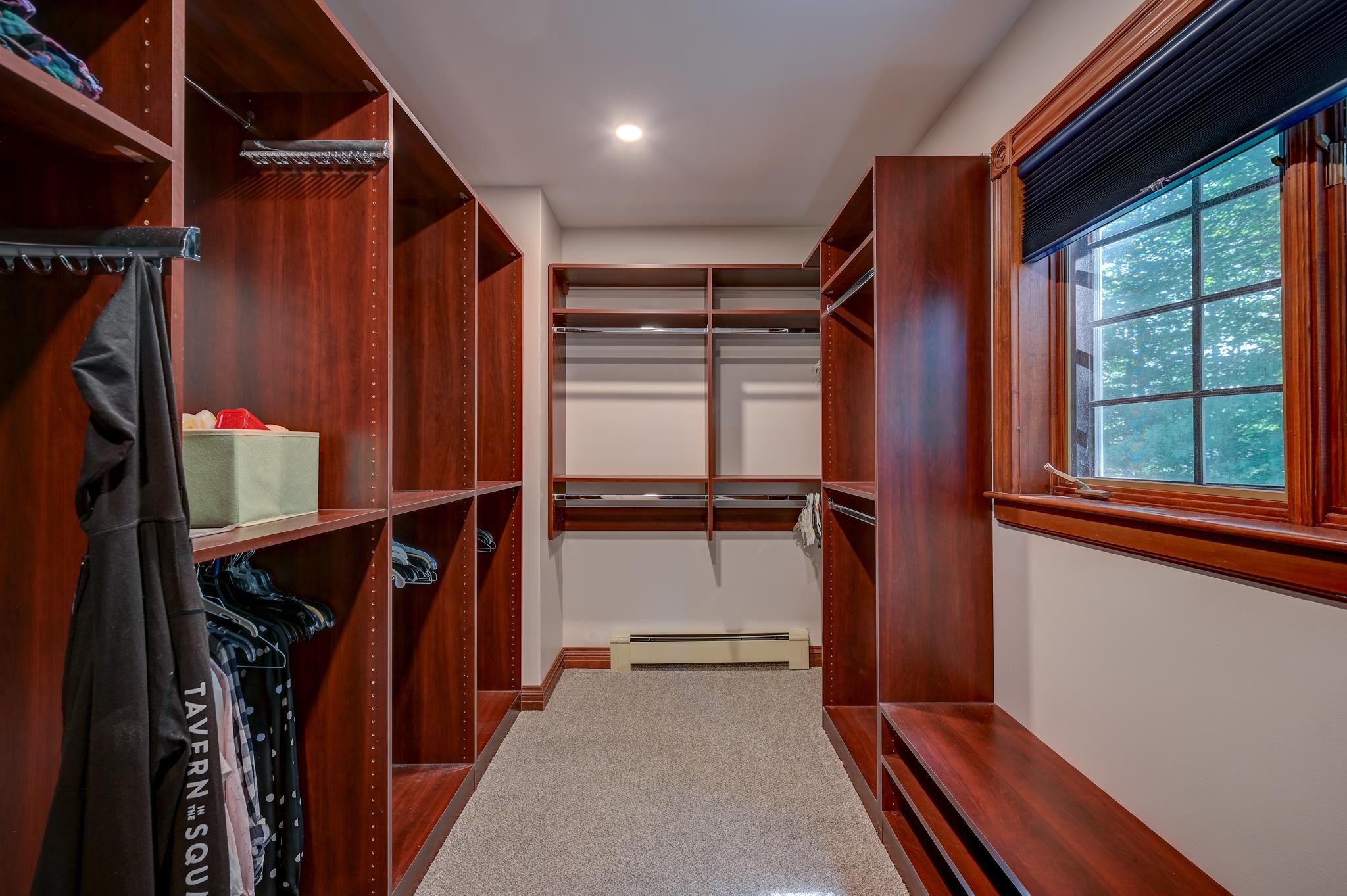 Walk-in closet with rich wood shelving, hanging clothes, and a large window.