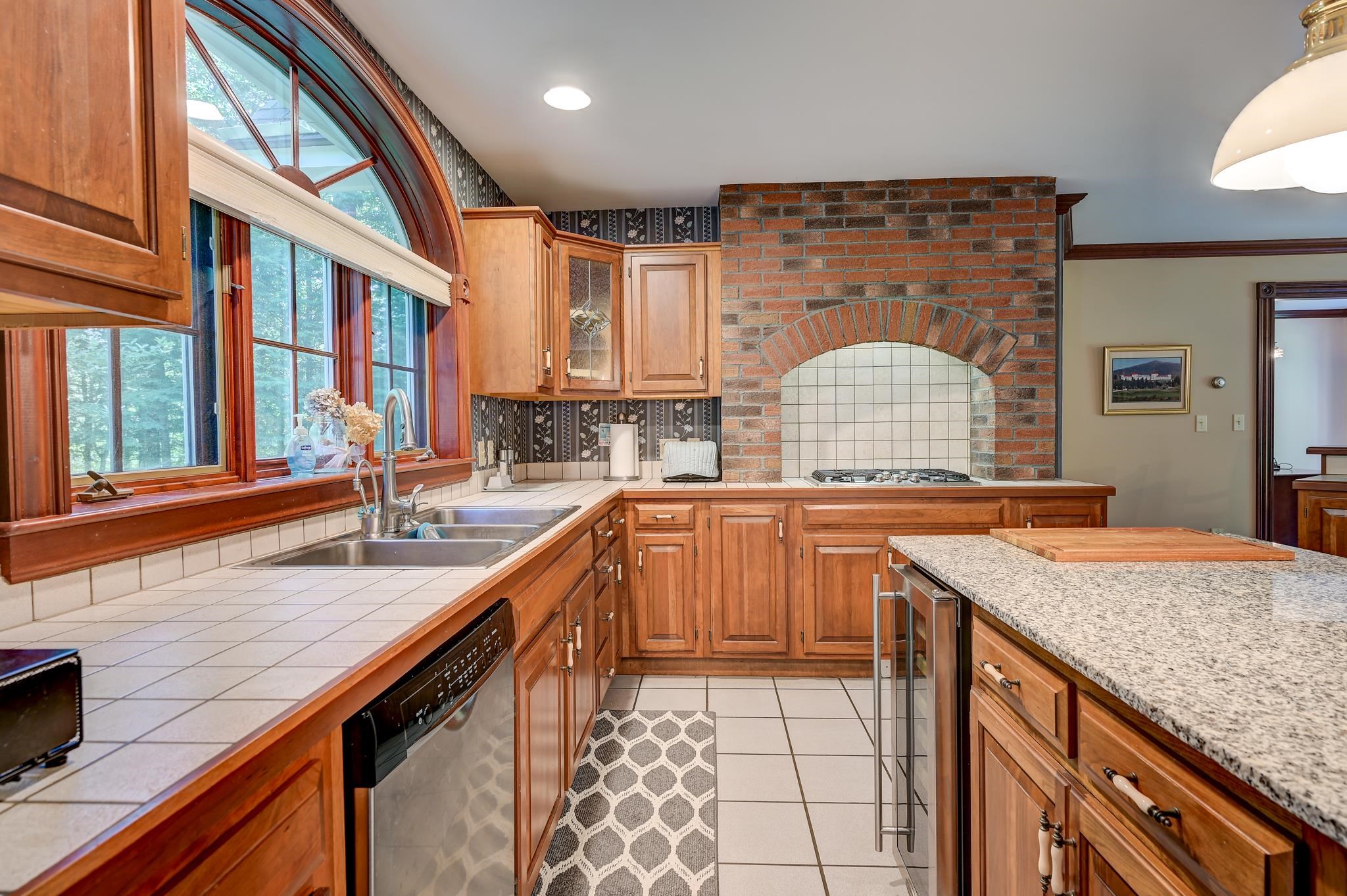 Kitchen with warm wood cabinets, a brick cooking alcove, and a large arched window.