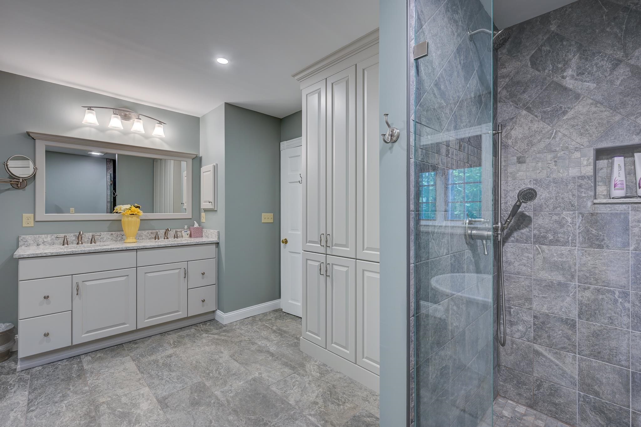 Bathroom with a white double vanity, built-in cabinetry, and a glass-enclosed tiled shower.