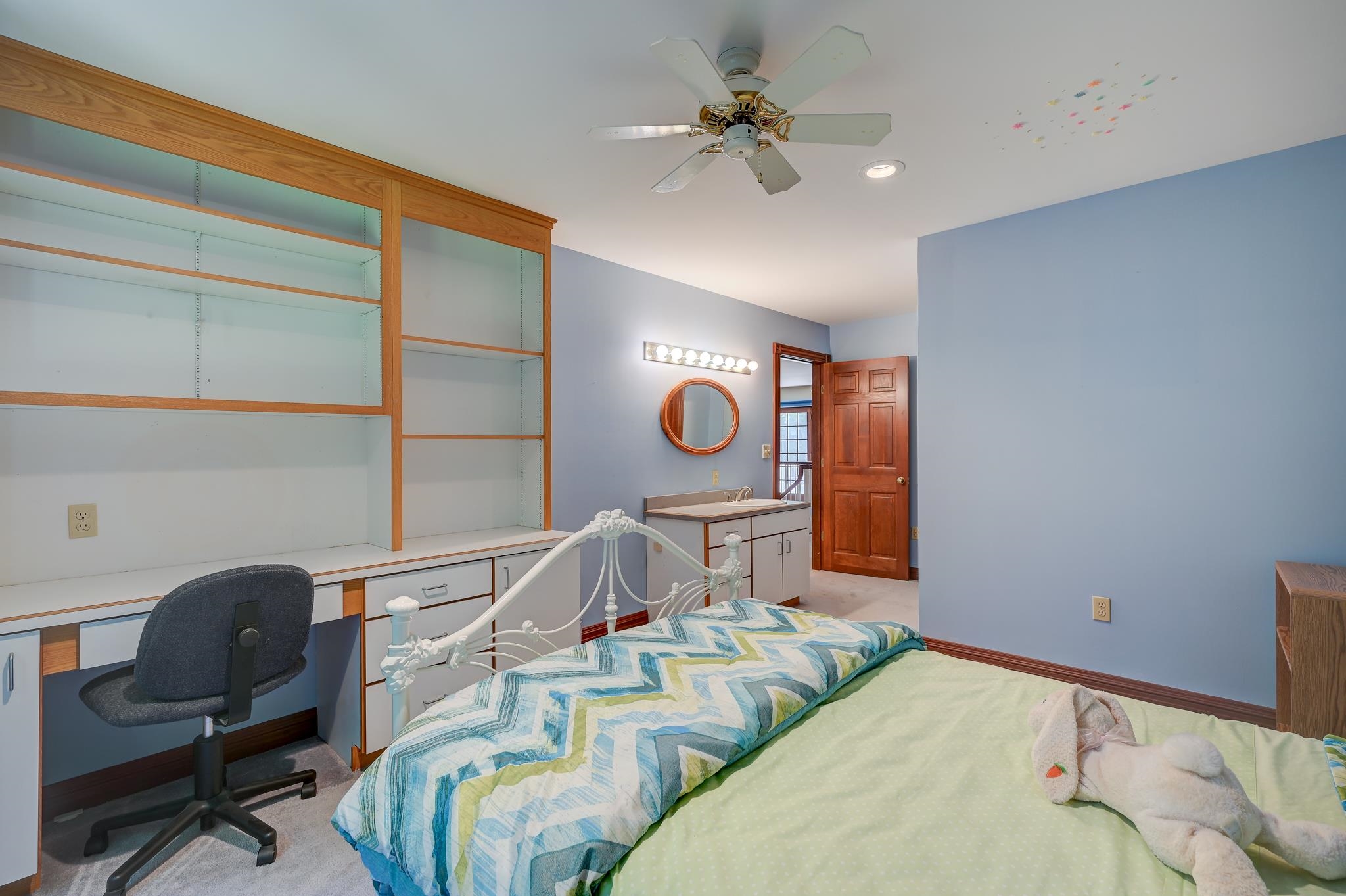 Bedroom with built-in desk and shelving, blue walls, and a white metal bed.