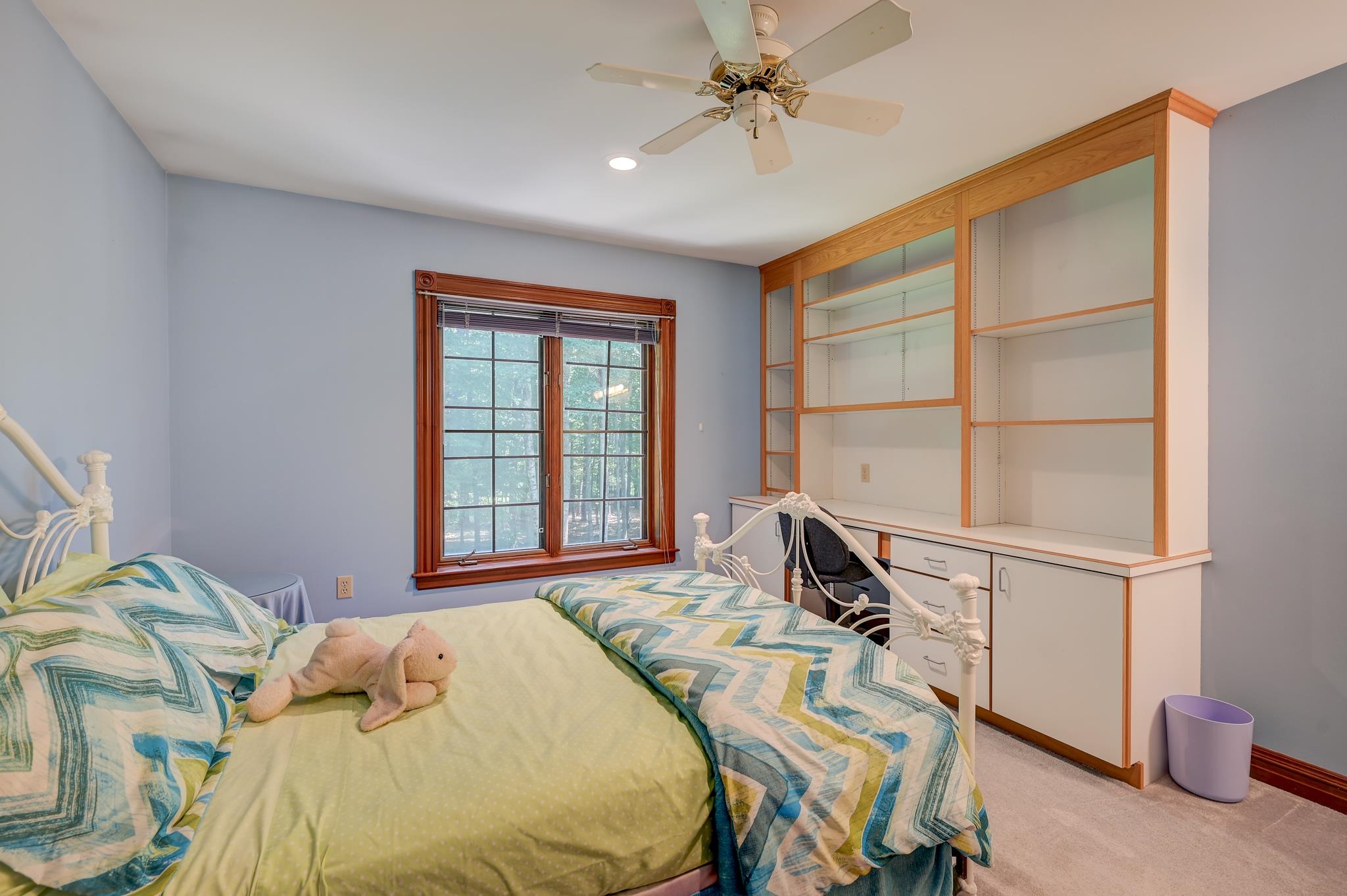 Bedroom with two beds, built-in desk and shelving, and a window overlooking trees.