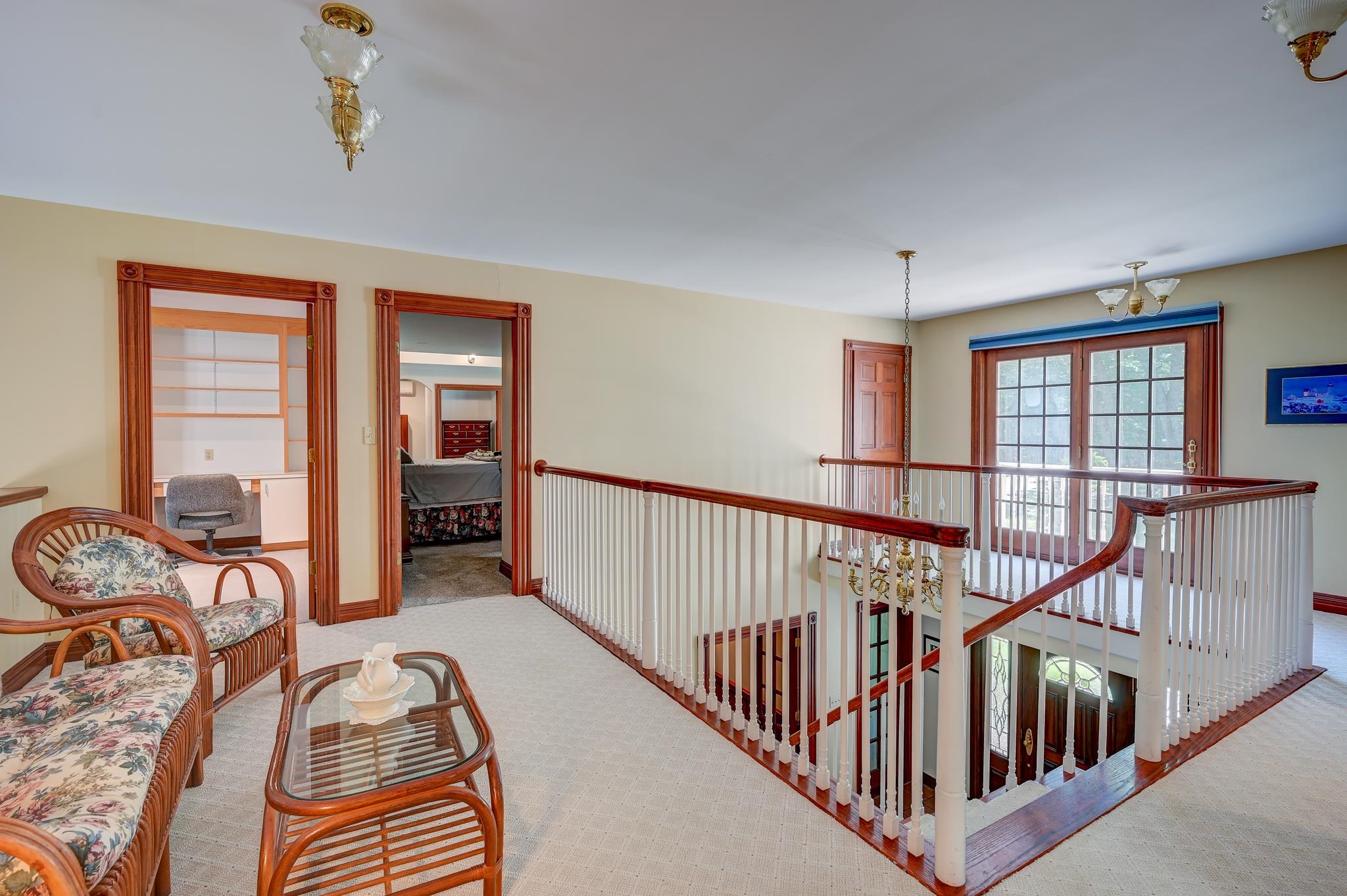 Upper-level landing with a wooden stair railing, wicker seating, and glass doors.