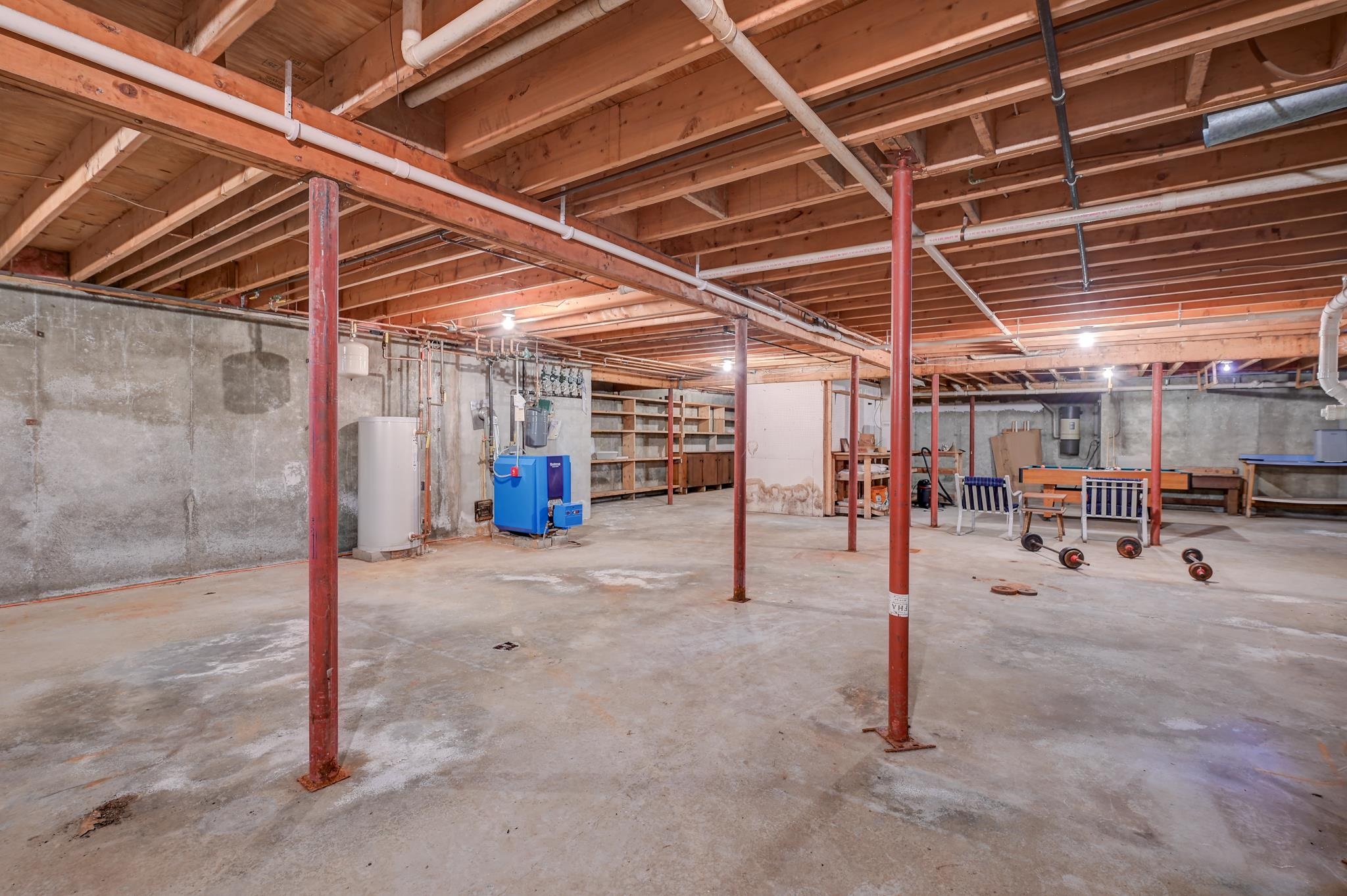 Unfinished basement with exposed ceiling beams, red support posts, and utility equipment.