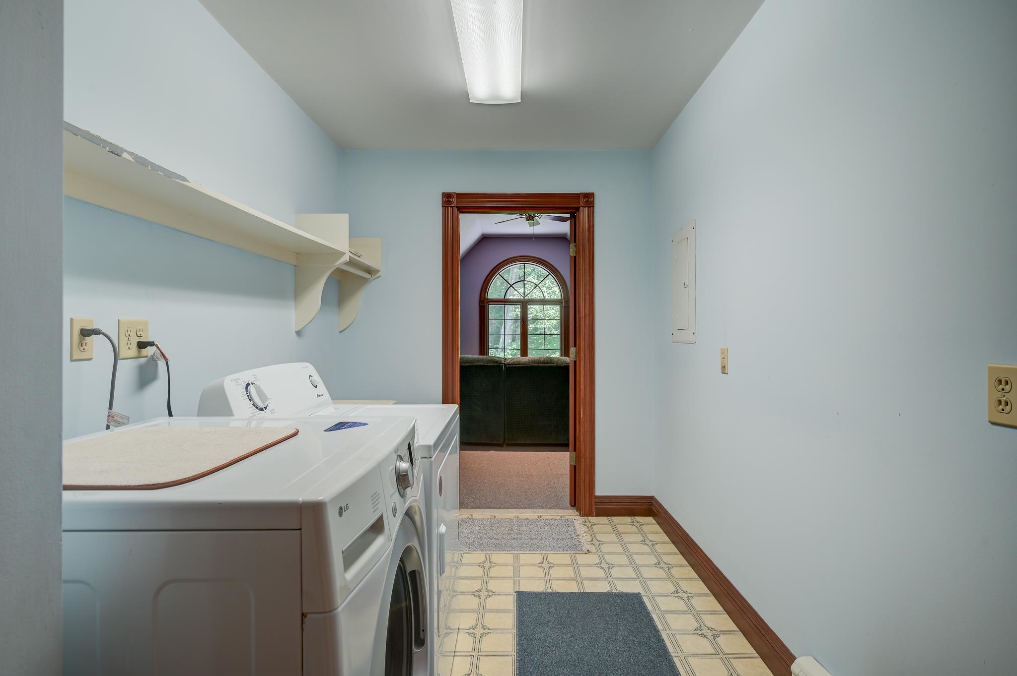Laundry room with washer and dryer, wall shelving, and doorway to an adjoining room with an arched window.