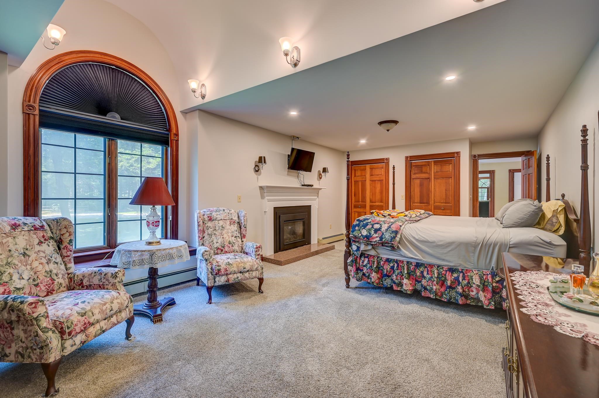 Bedroom with a sitting area, fireplace, and large arched window.