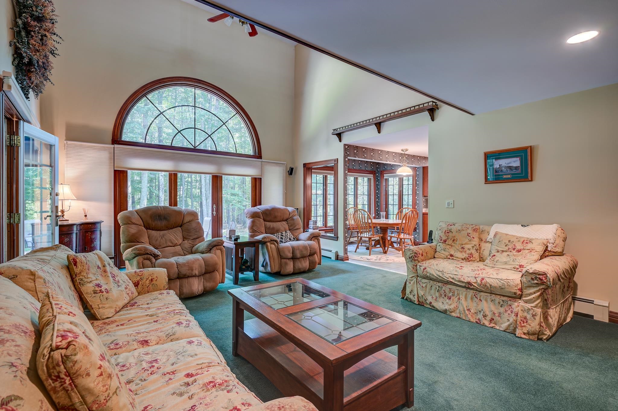 Living room with a vaulted ceiling, arched window overlooking trees, and floral sofas.