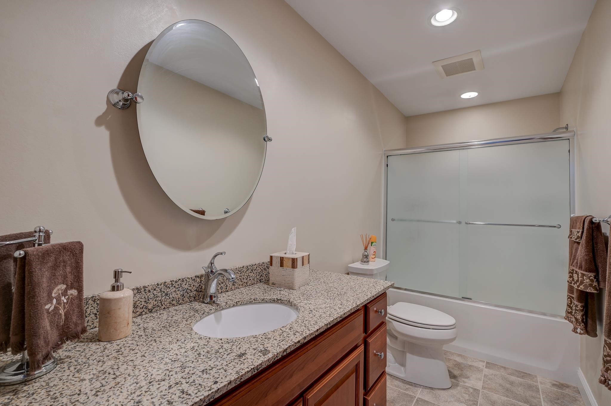 Bathroom with granite vanity, oval mirror, toilet, and frosted sliding tub doors.