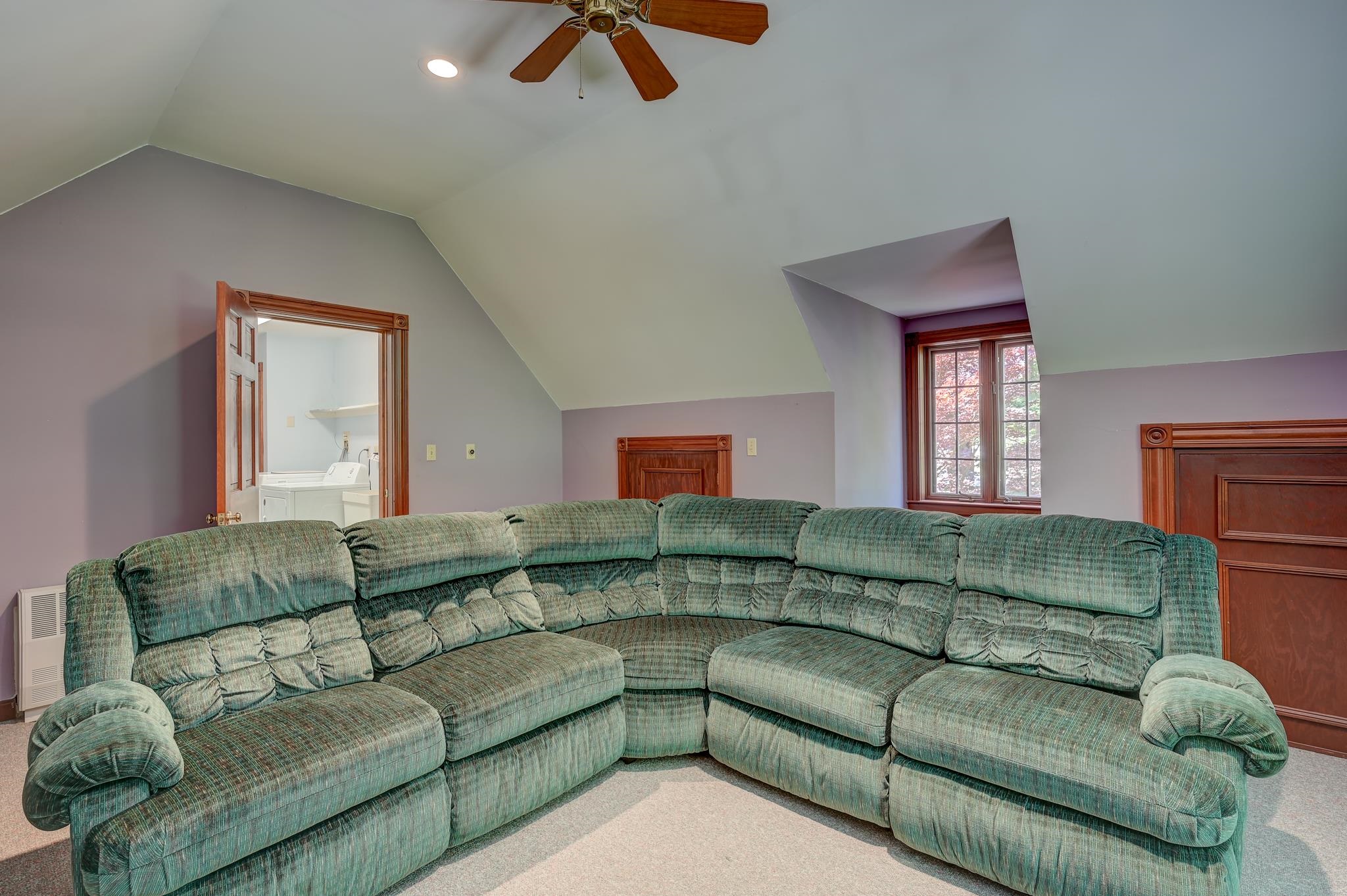 Furnished living room with a large green sectional beneath a sloped ceiling.