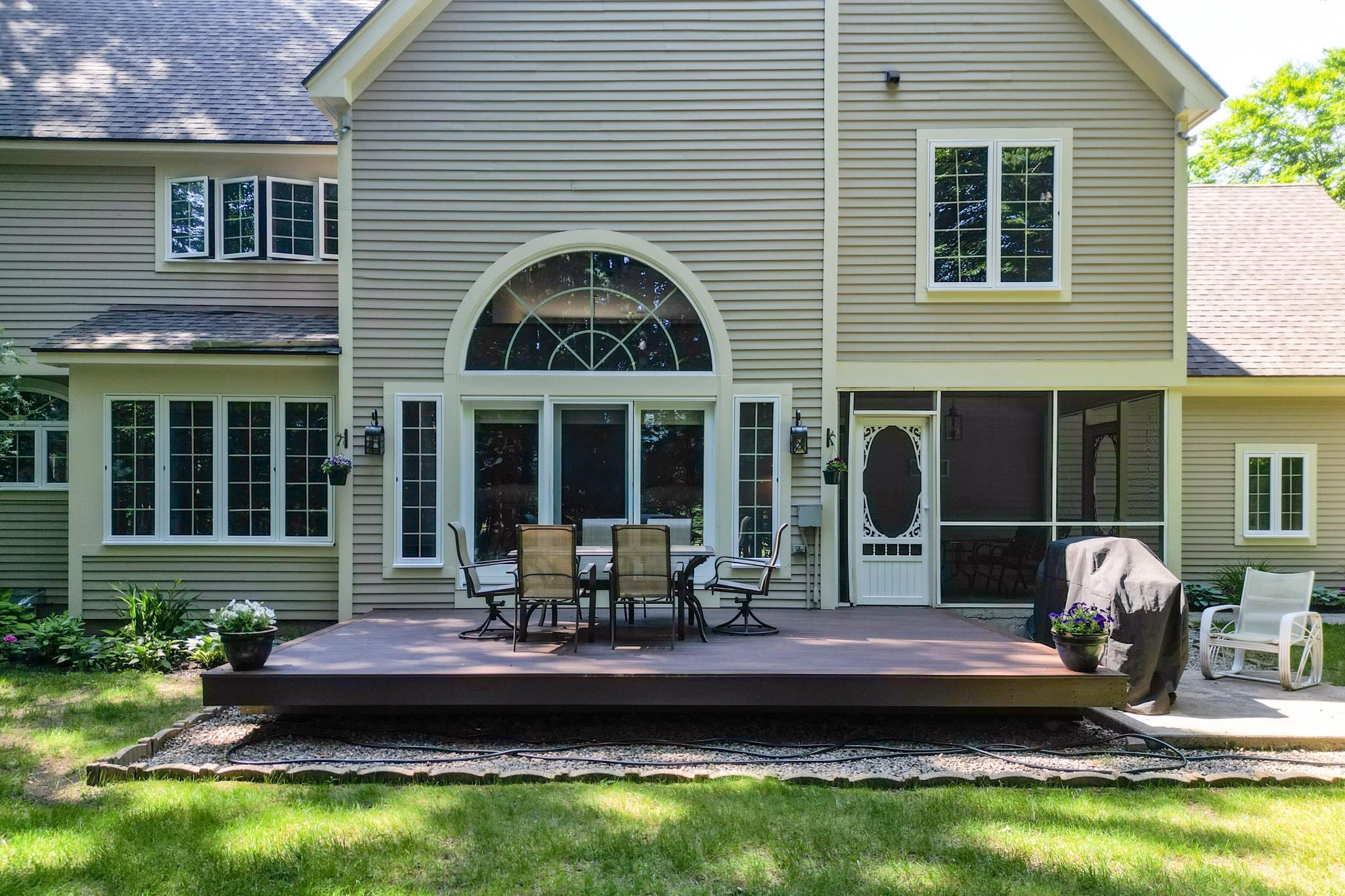Rear of a gray-sided house with a broad deck, arched window, and screened porch.