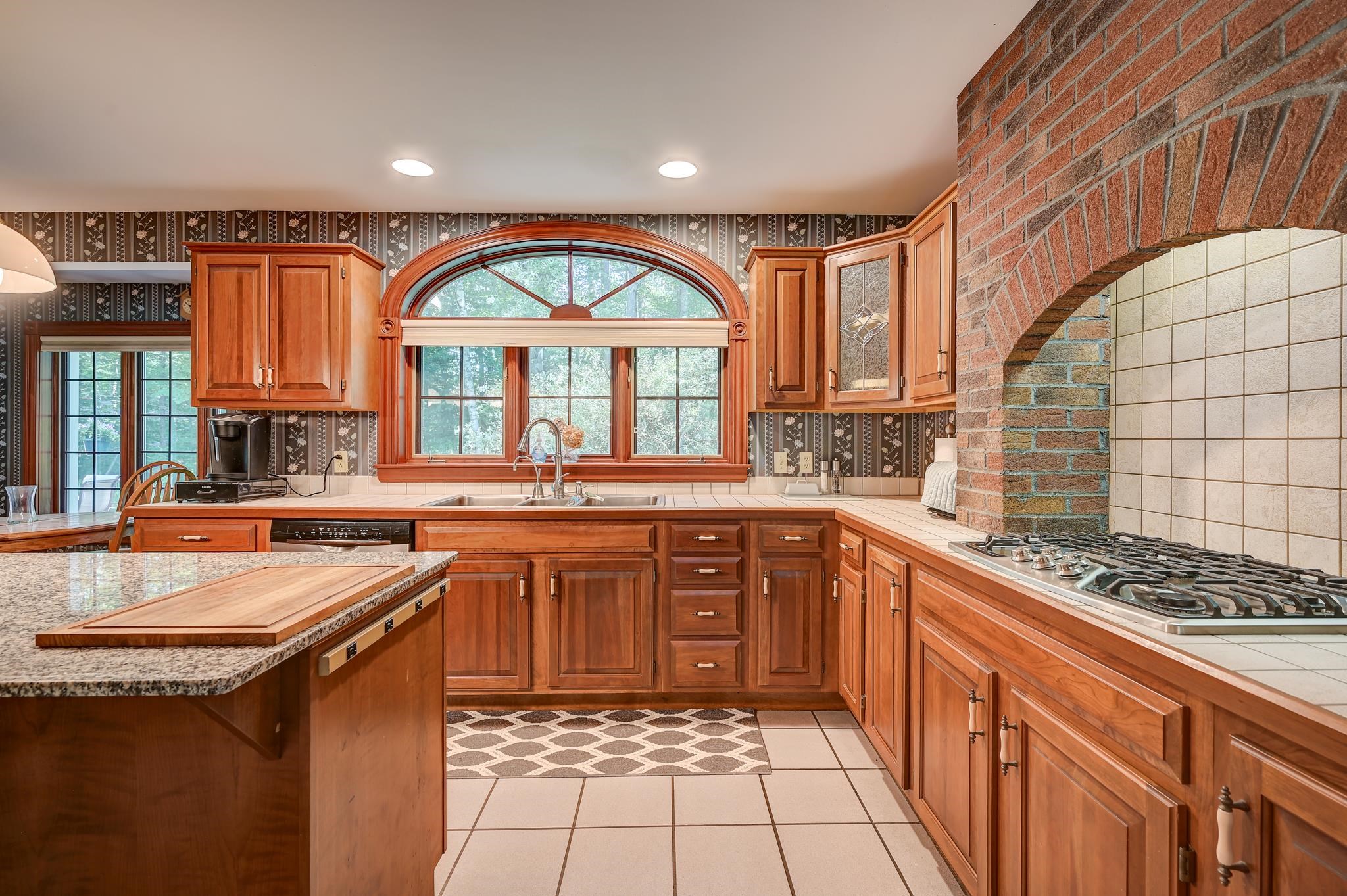 Kitchen with warm wood cabinetry, an arched window, and a brick cooking alcove with a gas range.
