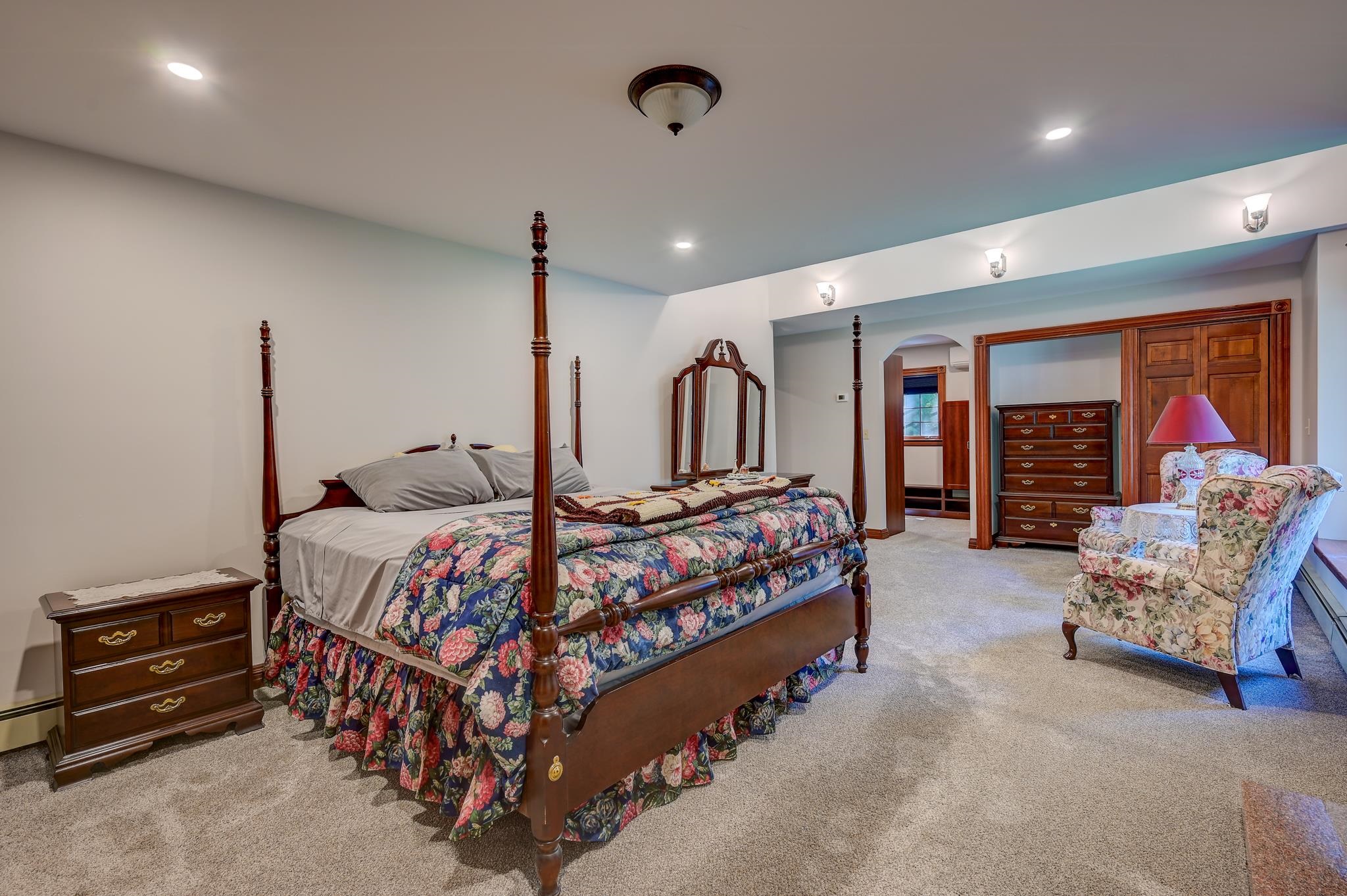 Bedroom with a carved four-poster bed, floral bedding, and a matching upholstered armchair.