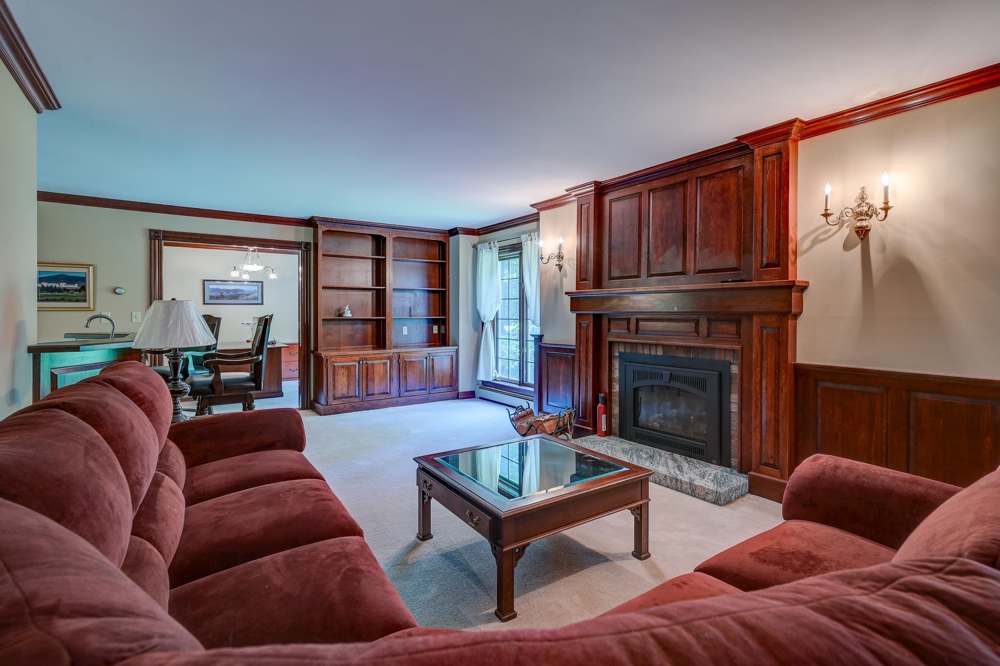 Living room with a large wood-paneled fireplace, built-in shelves, and burgundy sofas.
