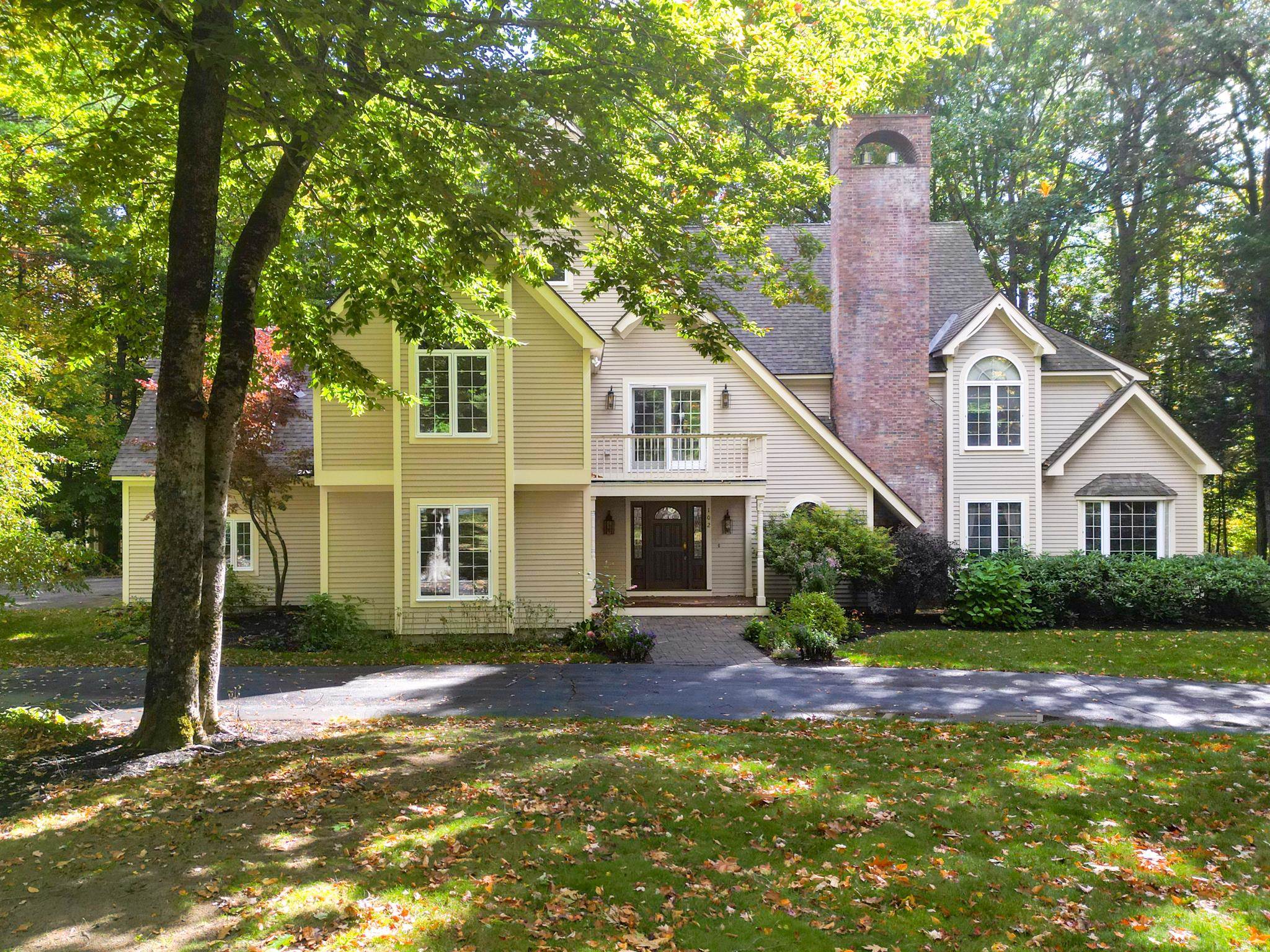 Front exterior of a two-story home with a tall brick chimney, framed by autumn trees.