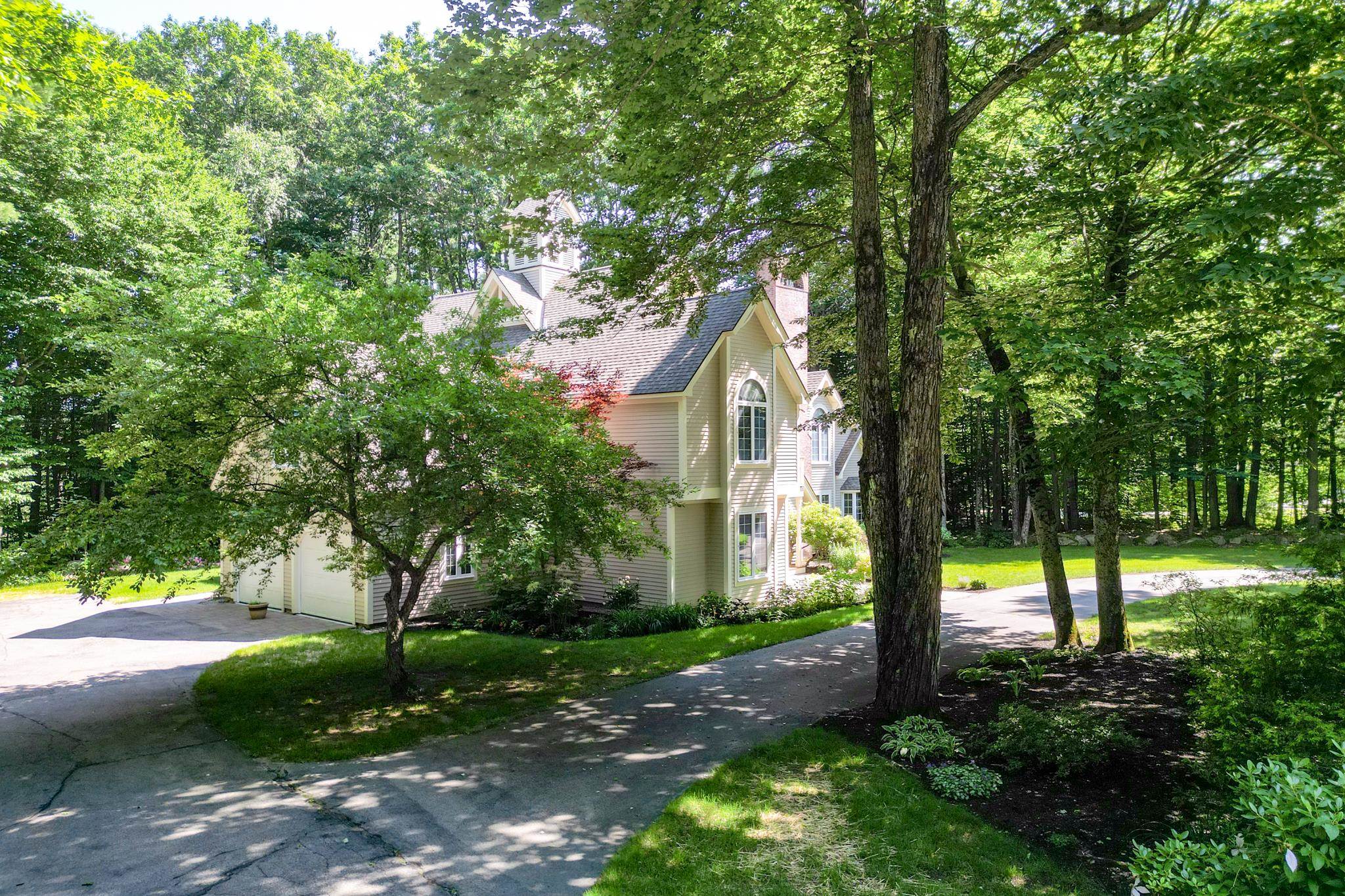 Light-colored multi-story home with an attached garage, framed by mature trees and gardens.