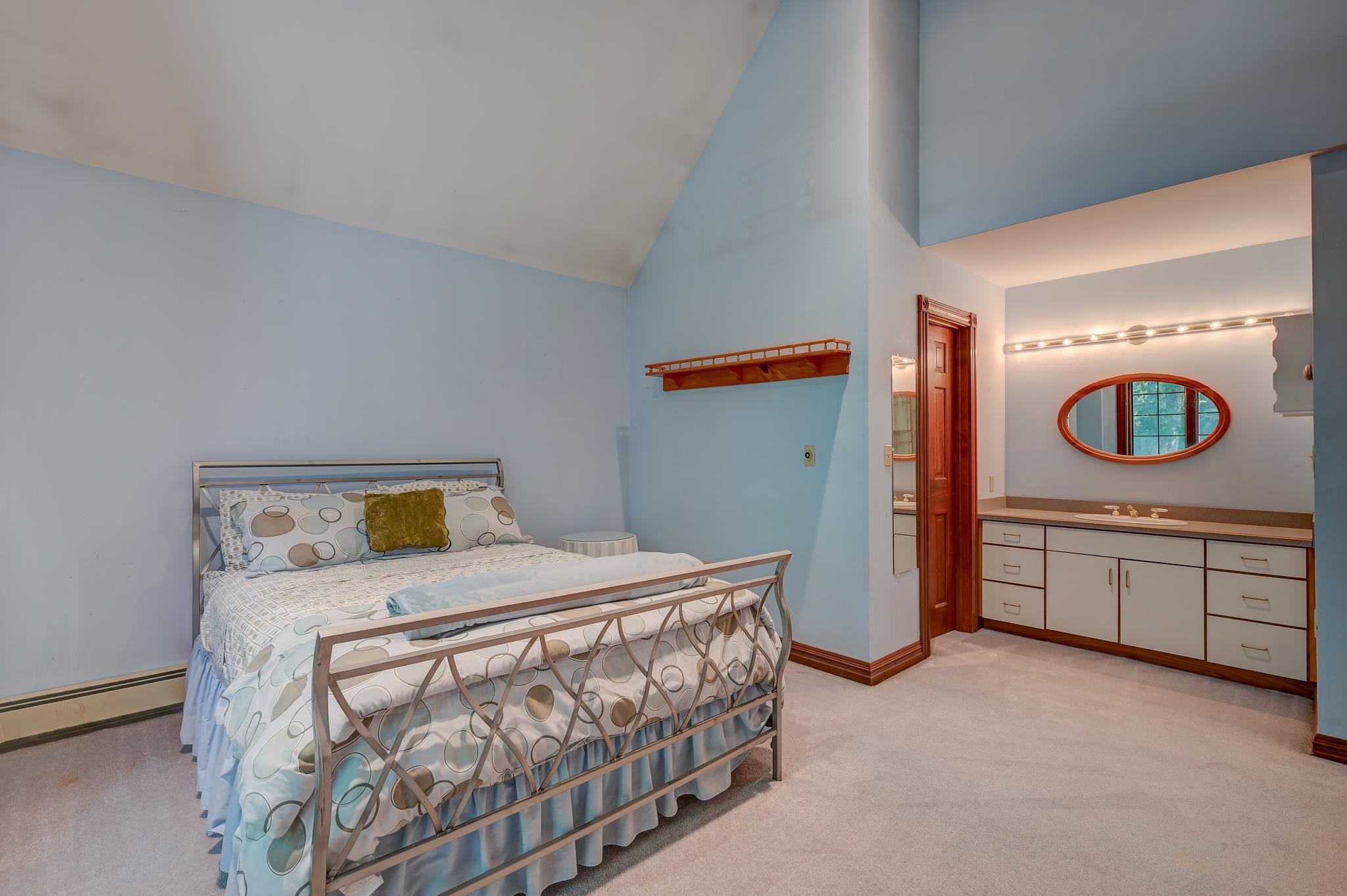 Bedroom with a metal-frame bed and adjoining bathroom vanity with an oval mirror.