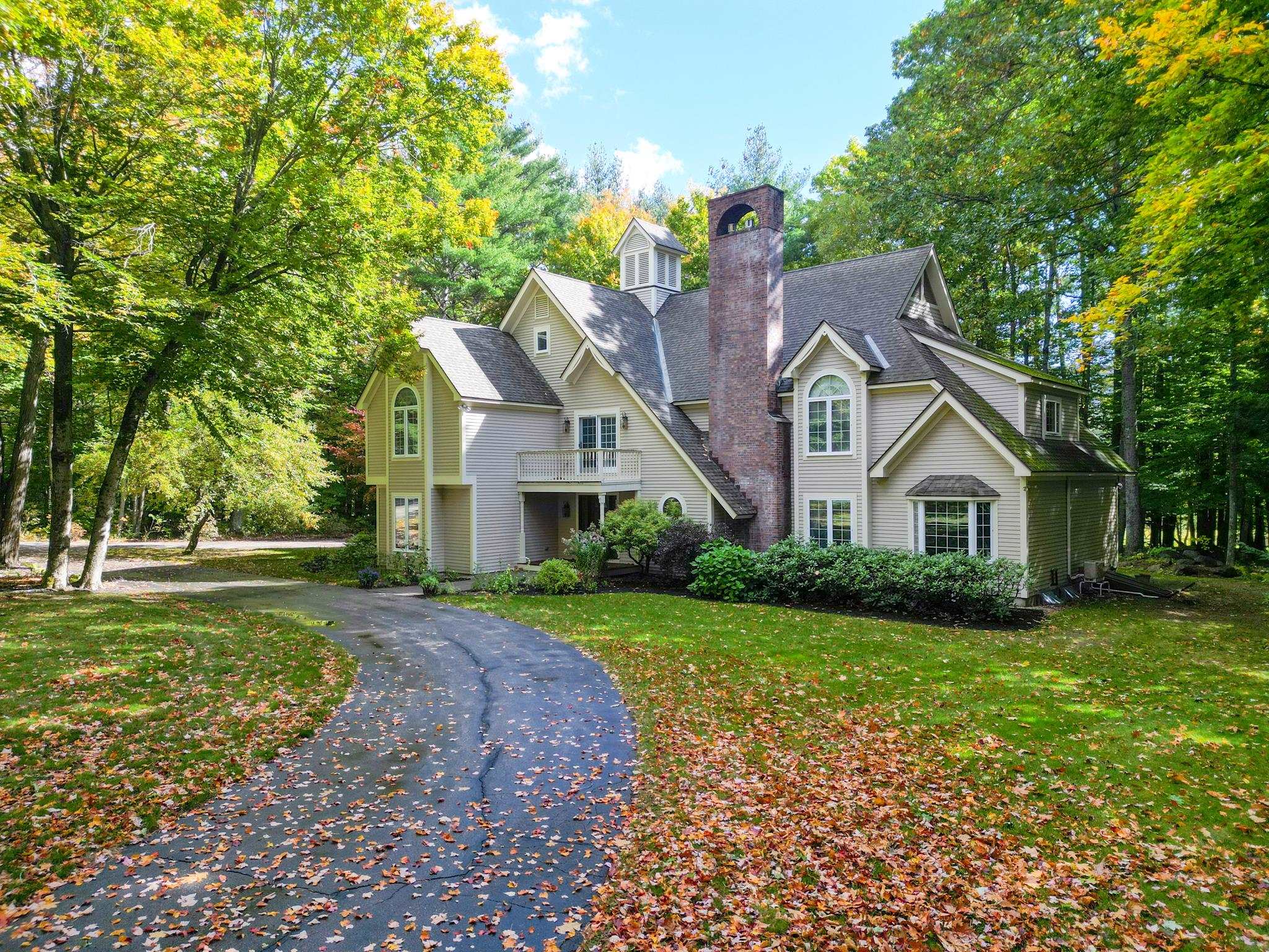 House with a brick chimney and cupola, set among autumn trees beside a curved driveway.