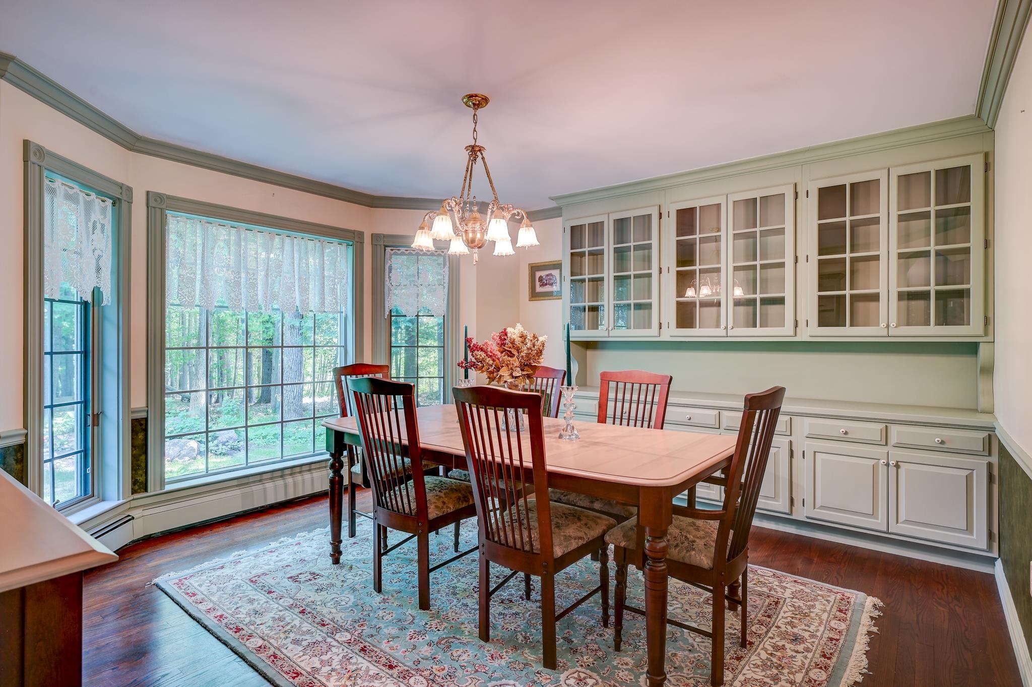 Dining room with a wooden table, built-in glass-front cabinets, and large windows overlooking trees.