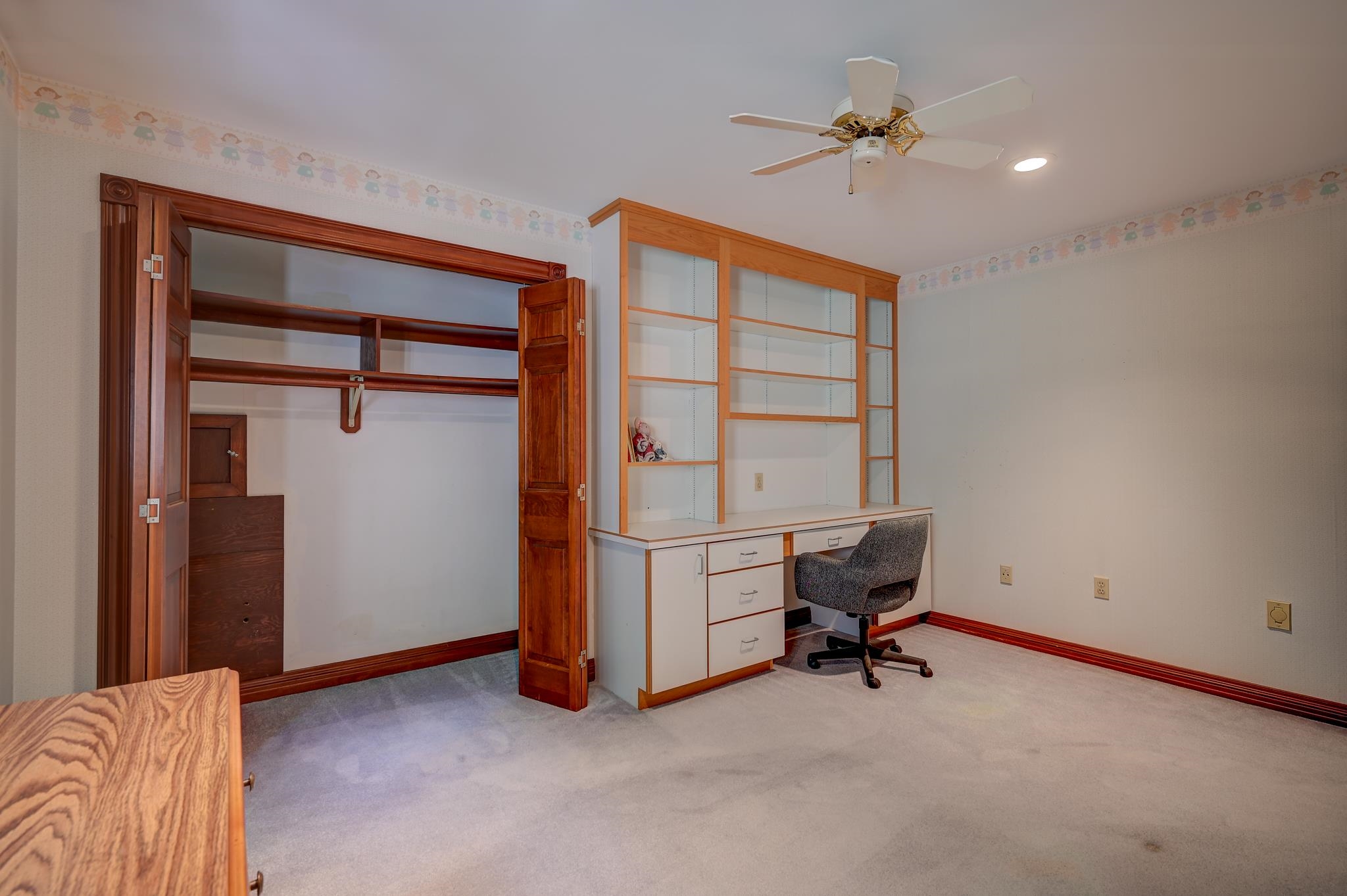 Home office with built-in desk and shelving beside a large closet with wooden doors.