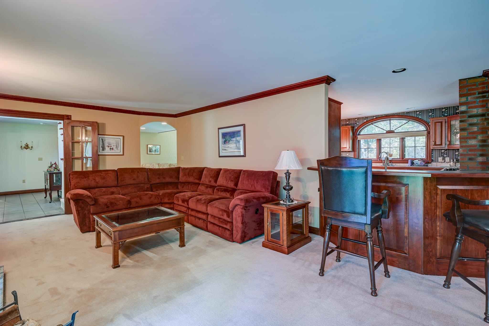 Living room with a red sectional sofa beside a wood-paneled kitchen bar and arched window.
