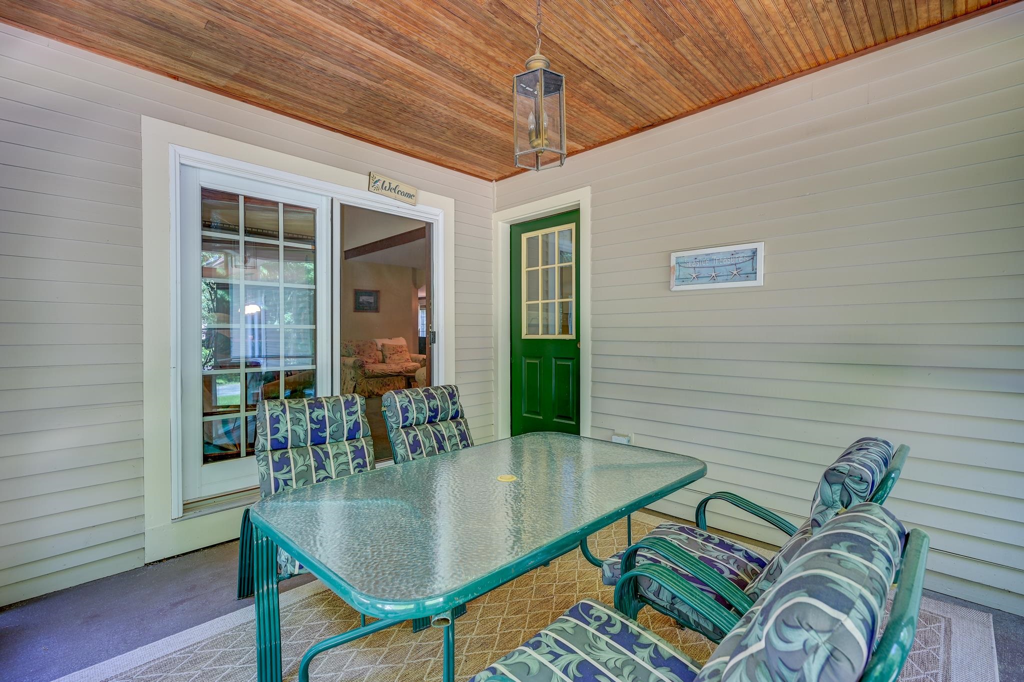 Covered porch with a glass-top patio table, cushioned chairs, and a green door.