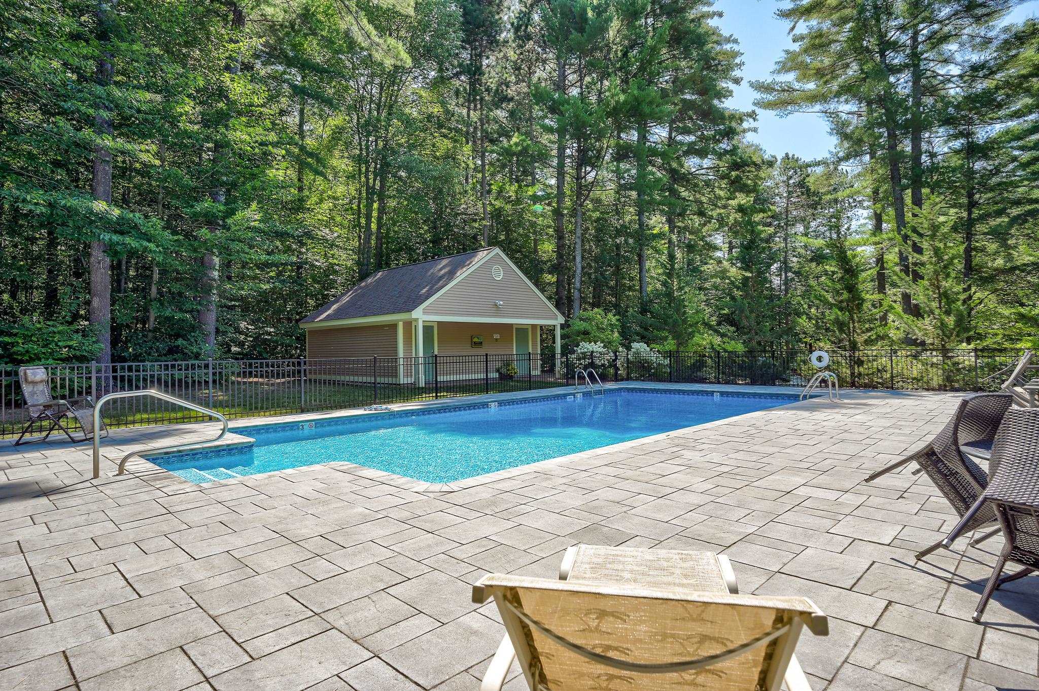 Outdoor swimming pool with a broad stone patio, lounge chairs, and a cabana beside the woods.