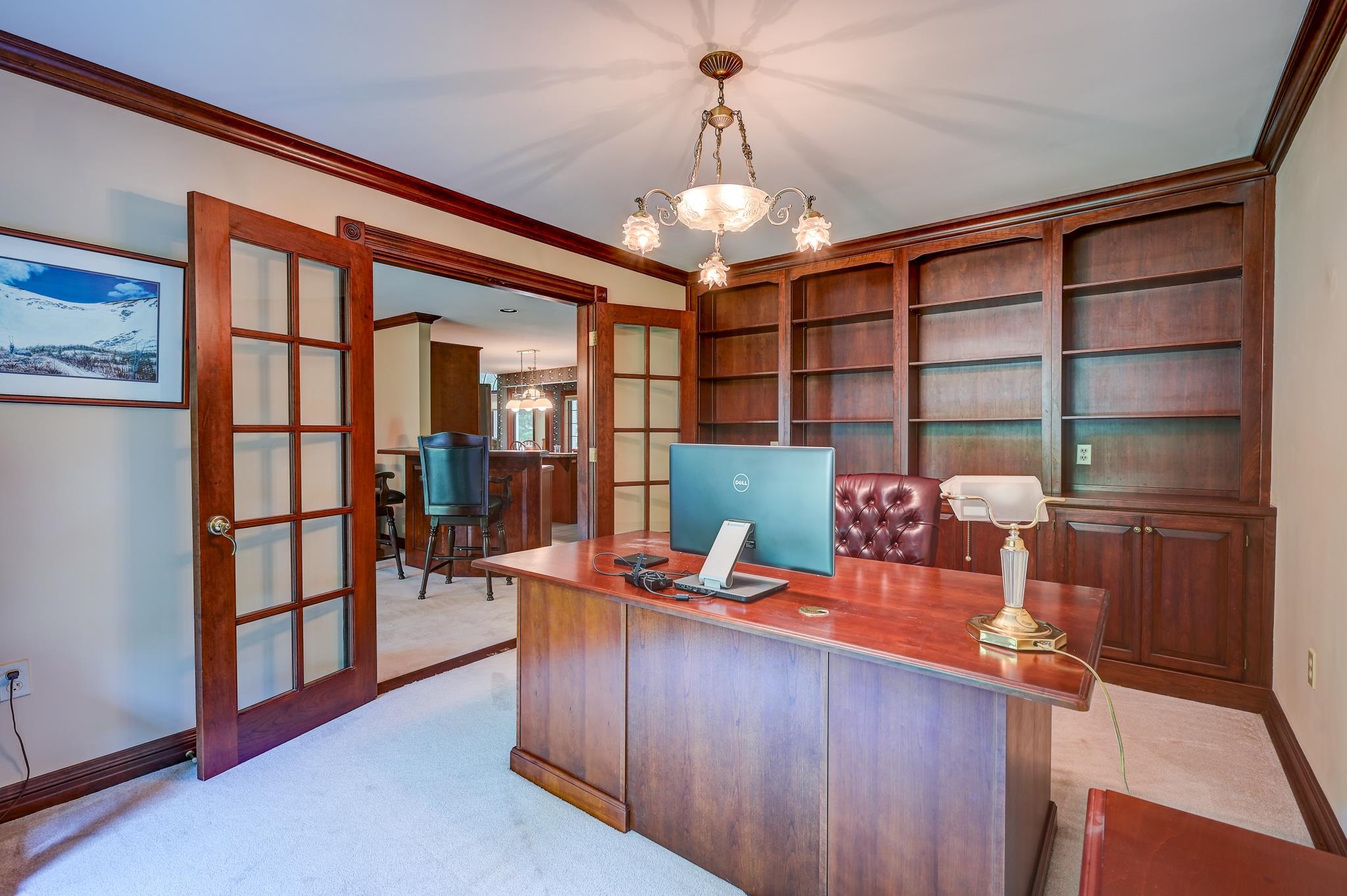 Home office with built-in wood bookshelves, a large desk, and glass-paneled doors.