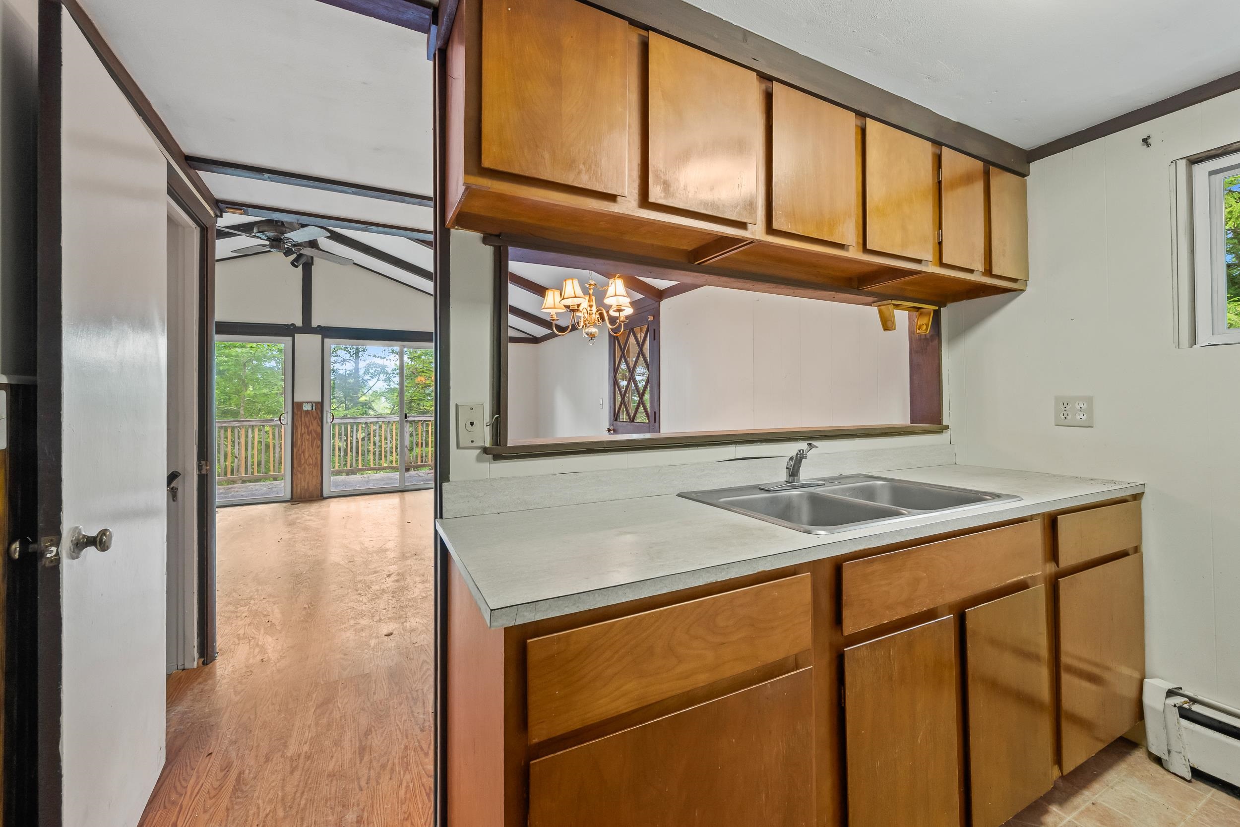 Kitchen with wood cabinets and double-basin sink, opening to a vaulted living area with deck access.