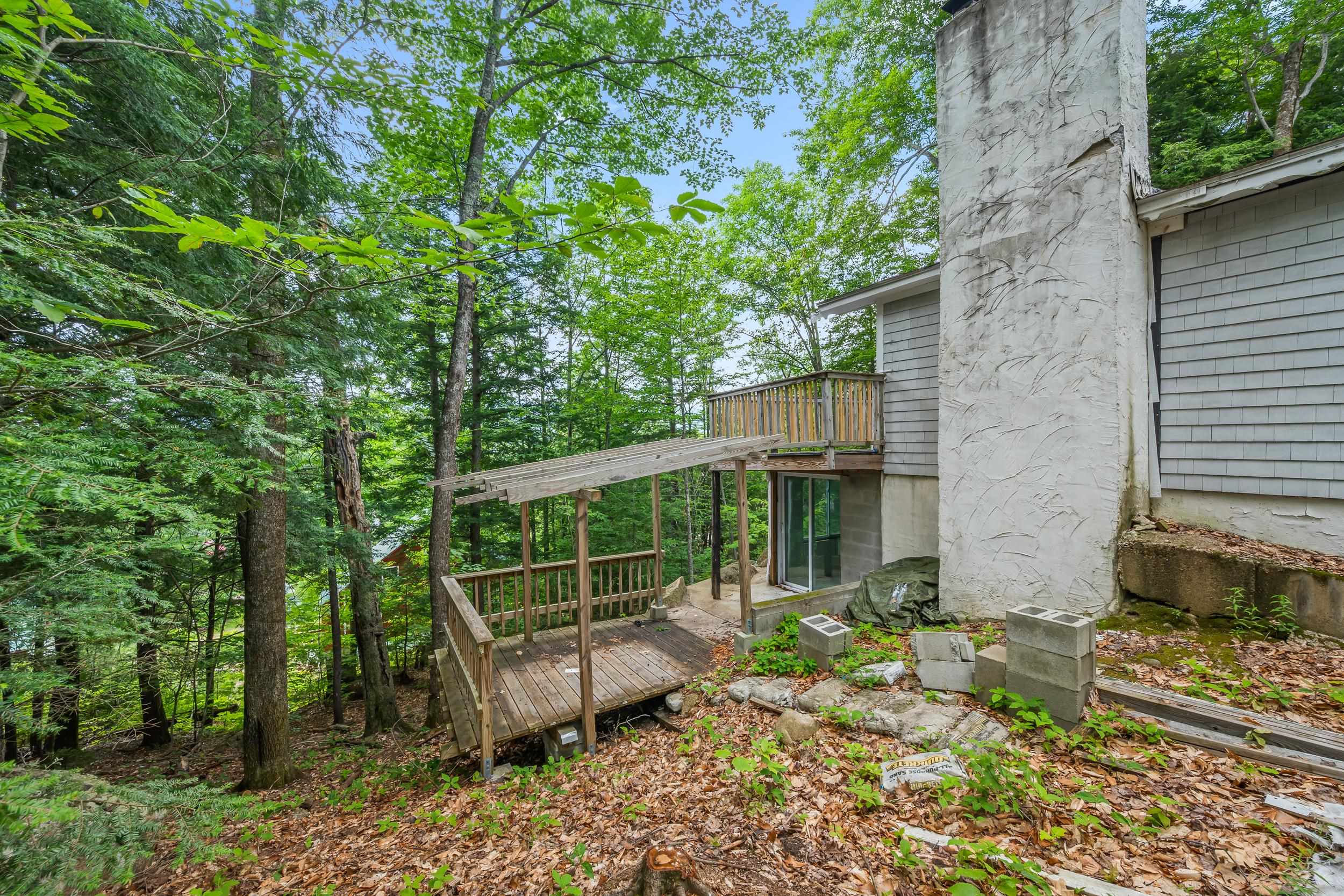 Wooded home exterior with a raised wooden deck, ramp, and tall white chimney.