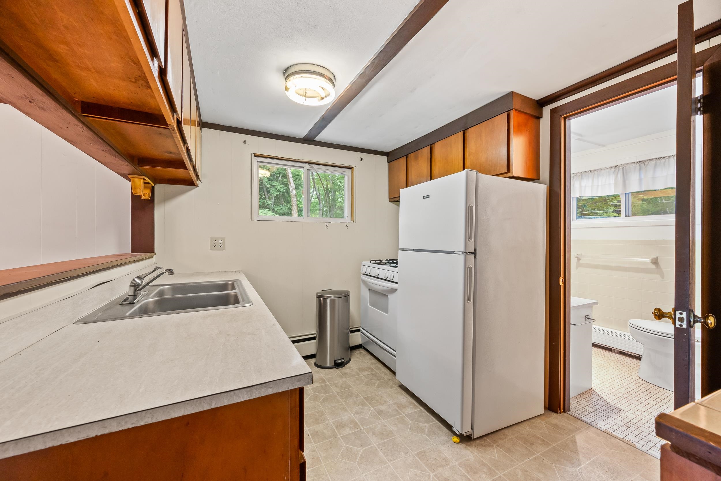 Kitchen with wood cabinets, a double-basin sink, and a refrigerator beside an open bathroom doorway.