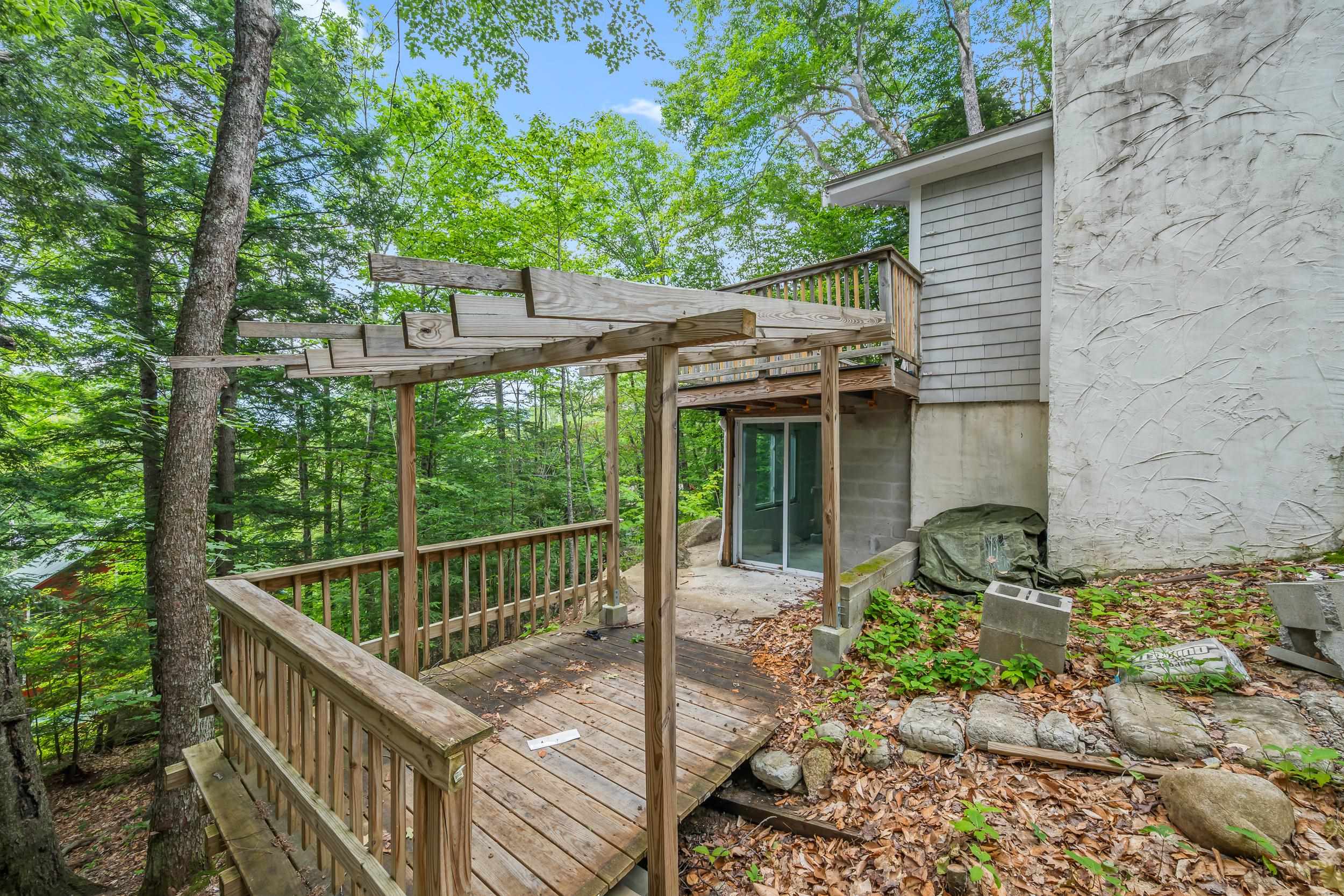 Wooden deck and unfinished pergola beside a wooded home.