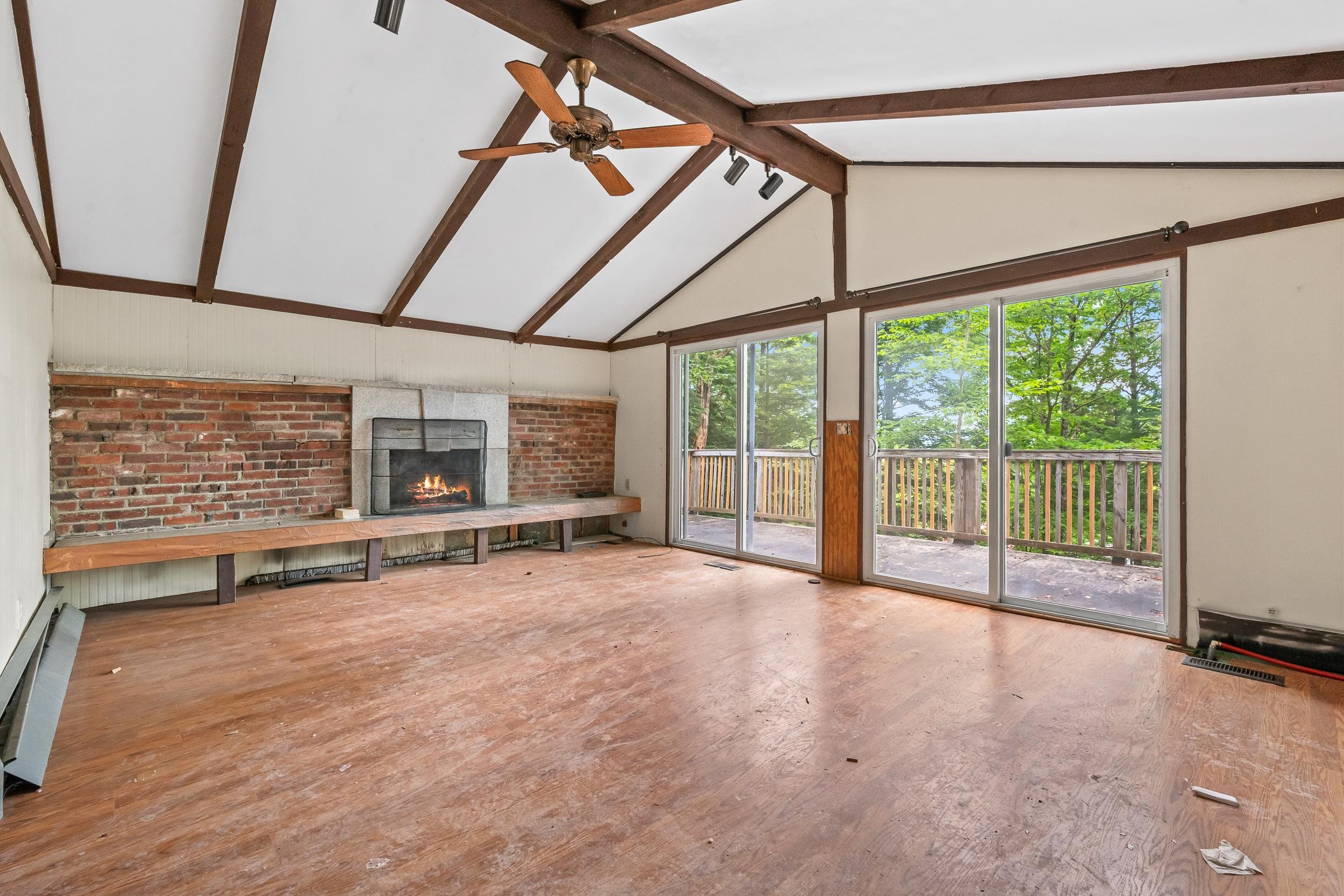 Living room with brick fireplace, vaulted exposed-beam ceiling, and sliding doors to a wooded deck.