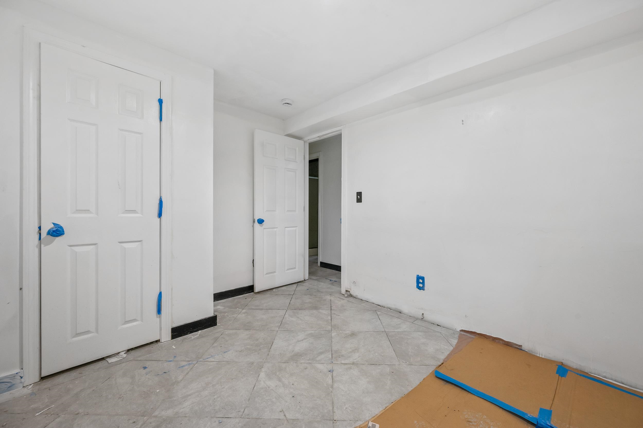 Unfinished room with gray tile flooring, two paneled doors, and cardboard protecting the floor.