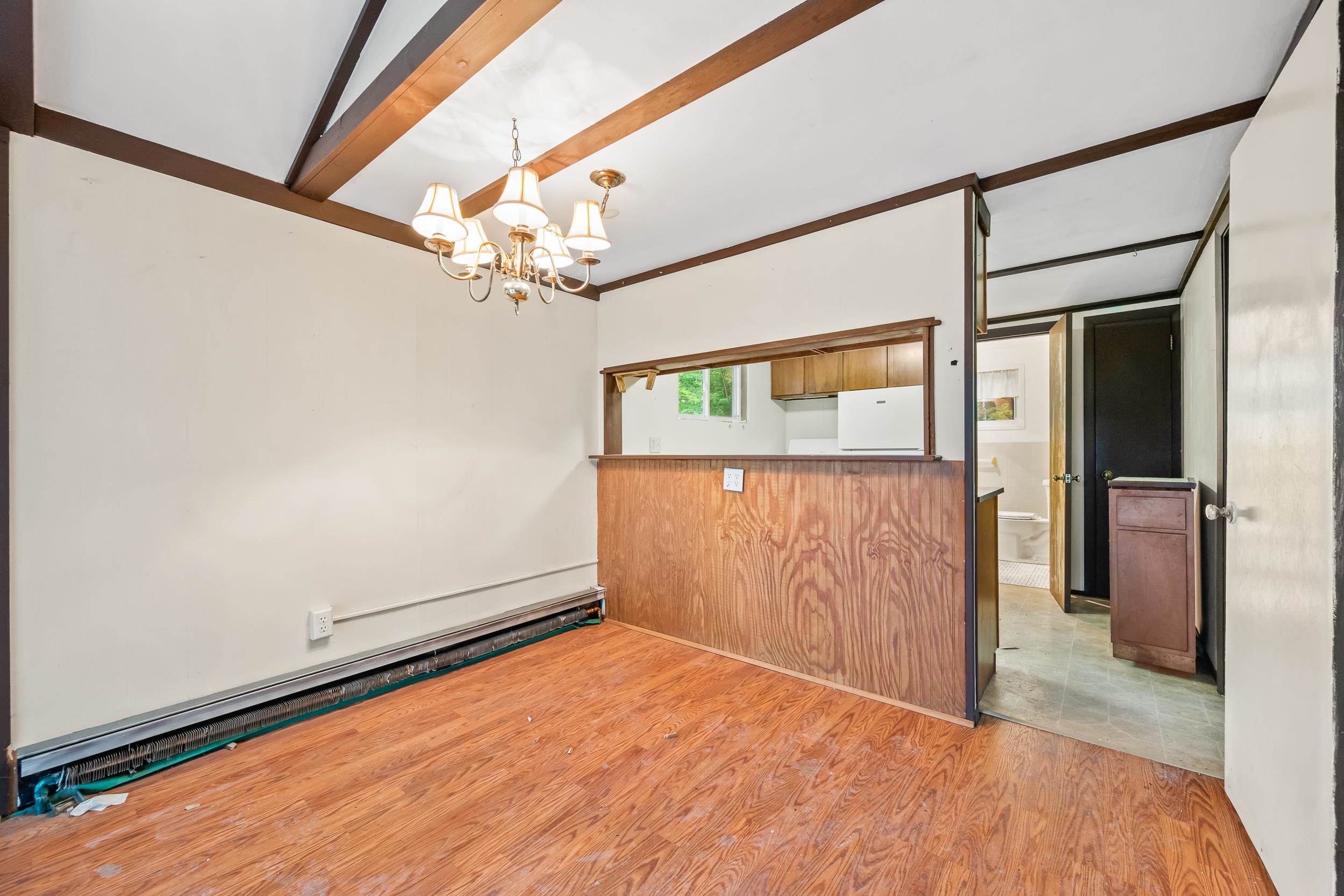 Dining area with exposed ceiling beams, a chandelier, and a wood-paneled kitchen pass-through.