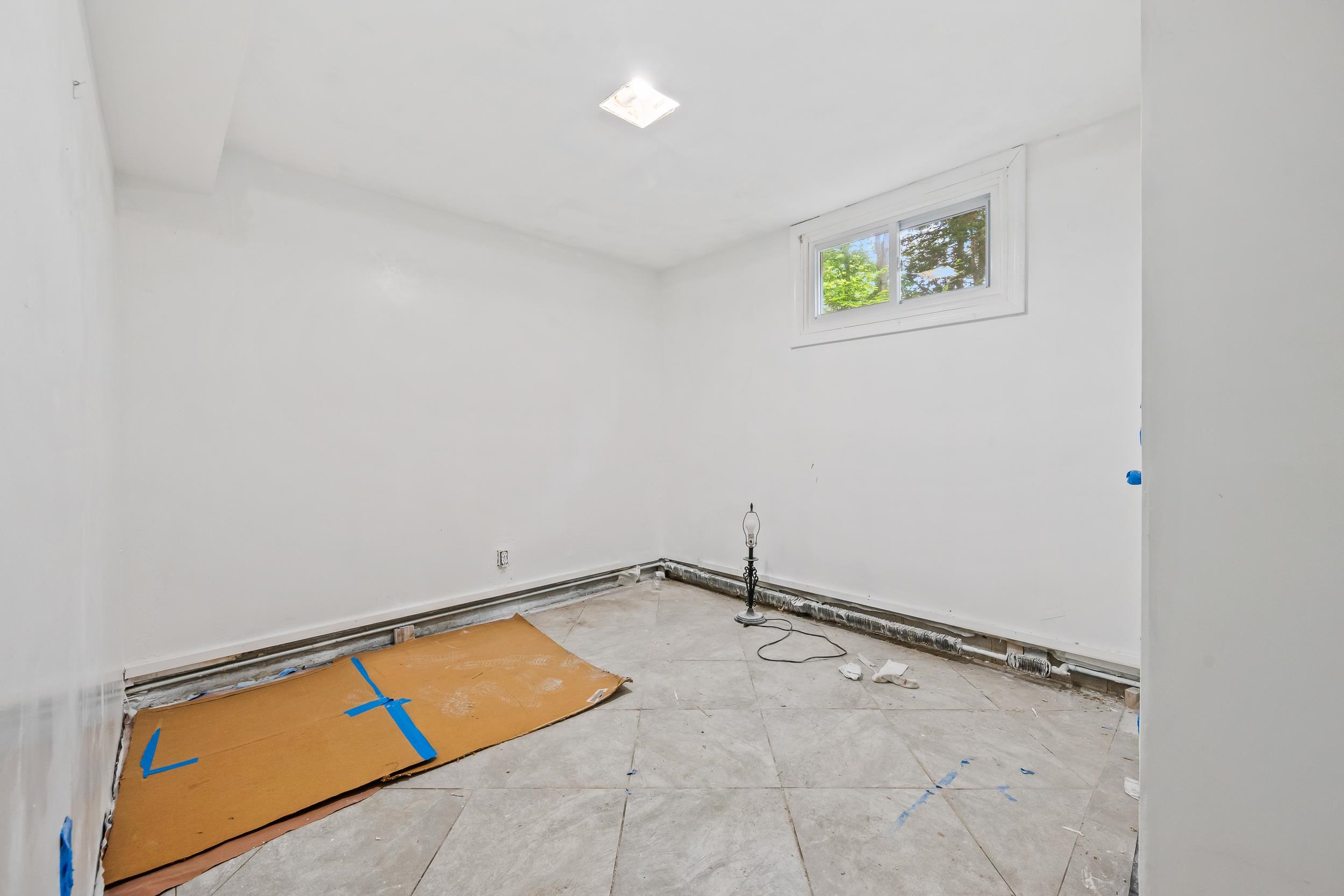 Unfinished room with tiled flooring, exposed work along the baseboards, and a small high window.