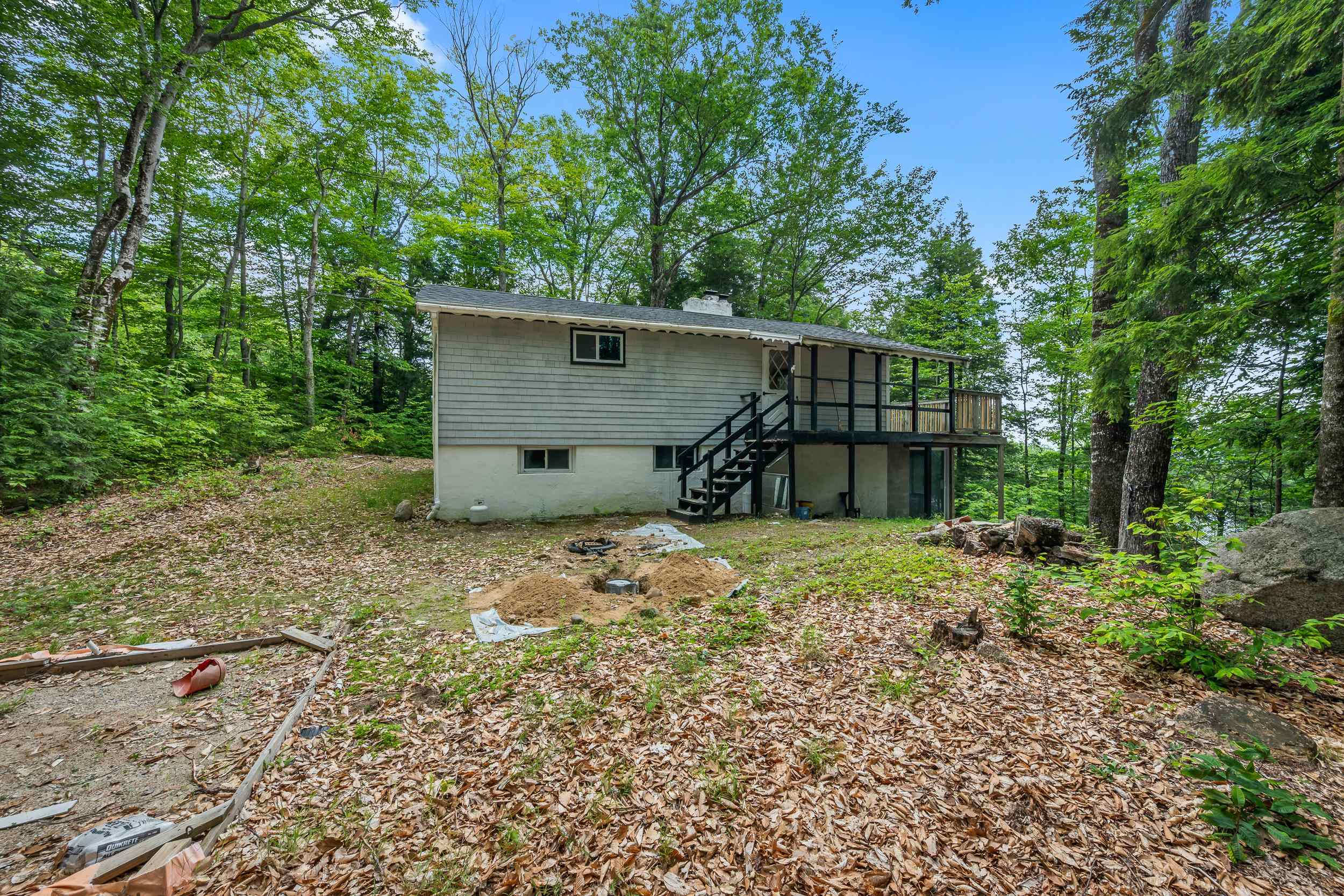 Raised house with an elevated deck and stairs in a wooded yard.