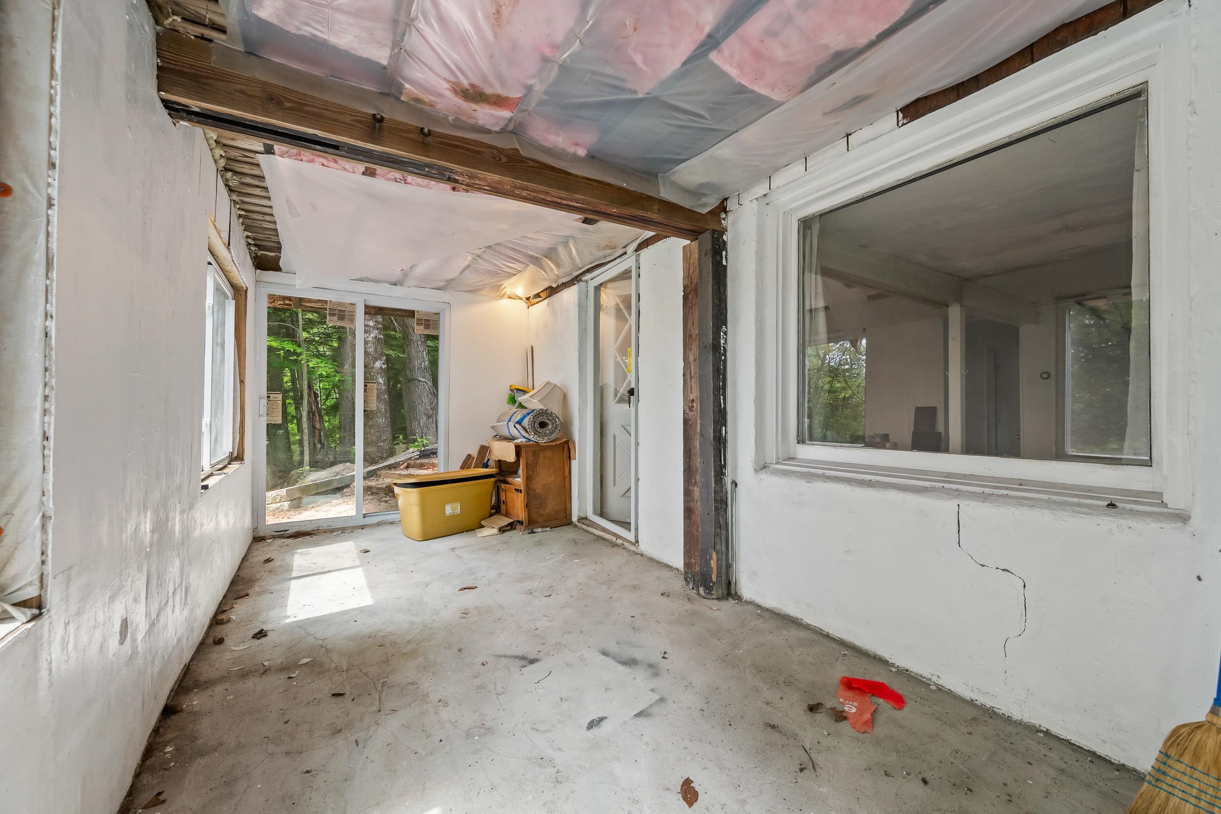 Unfinished room with exposed ceiling insulation, large windows, and sliding glass doors facing trees.