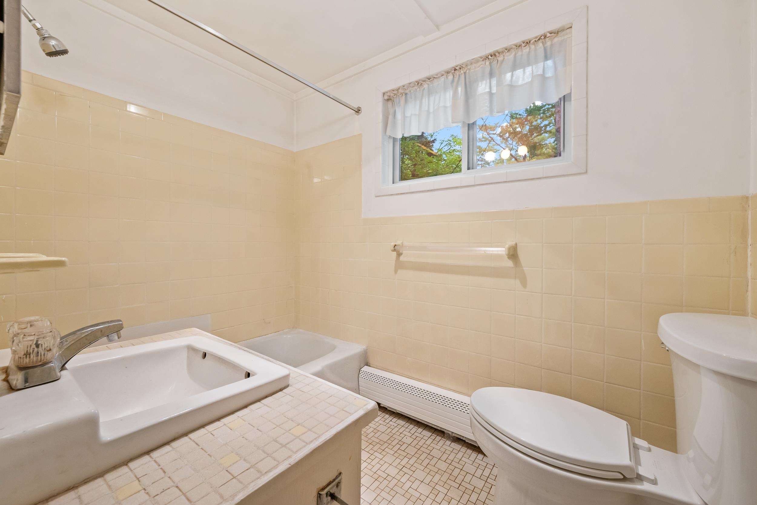 Bathroom with cream tile, a tiled vanity, bathtub, and high window overlooking trees.