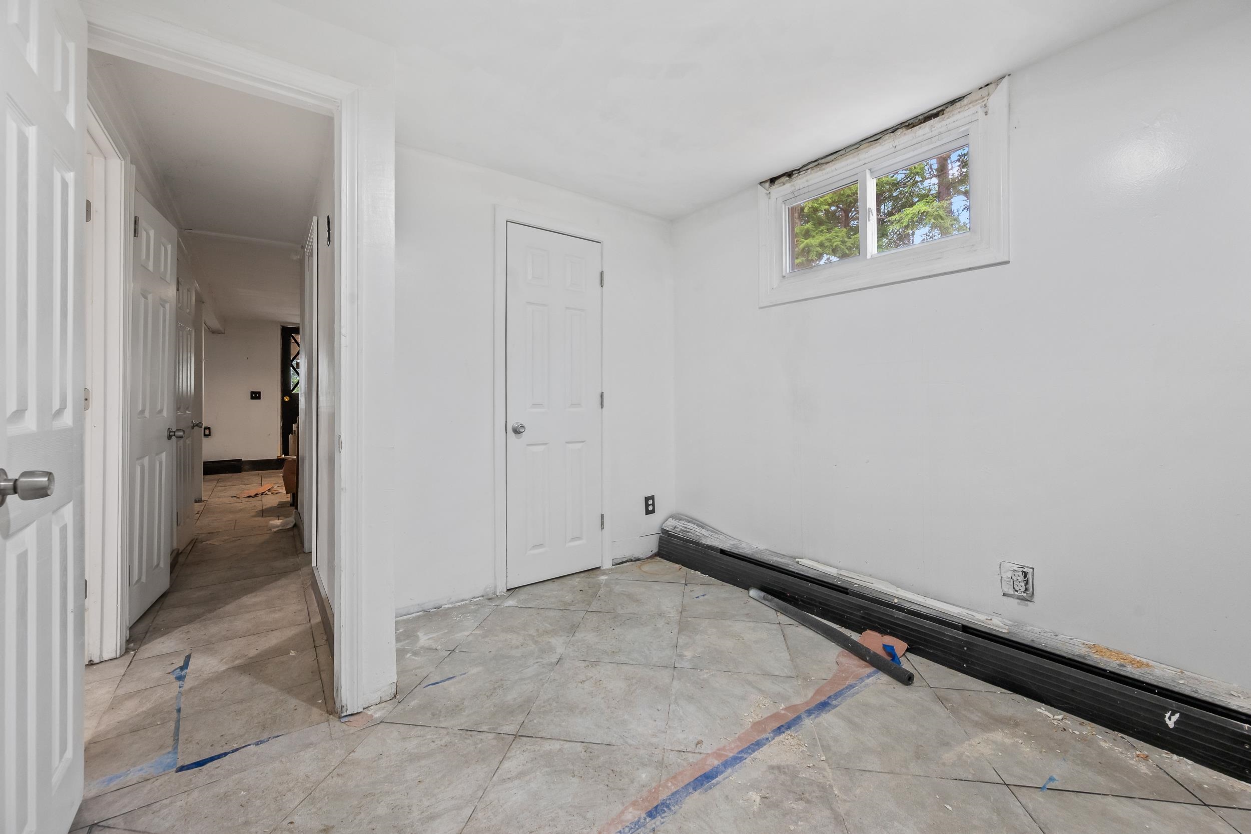Unfinished interior room with a high window, several doors, and construction materials along the wall.