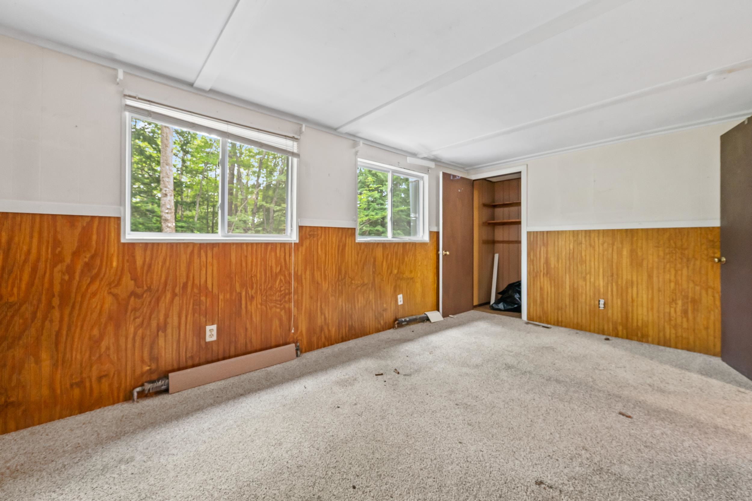Unfurnished room with wood-paneled walls, beige carpet, two windows, and an open closet.
