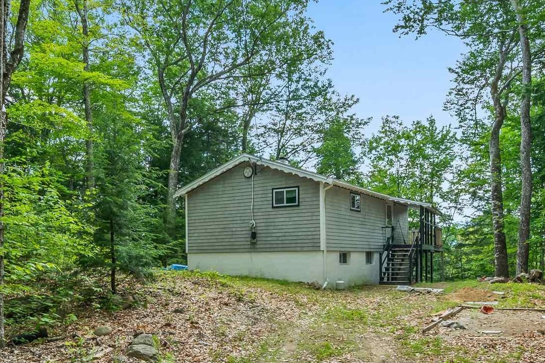 Gray-sided house with a raised deck and exterior stairs in a wooded clearing.