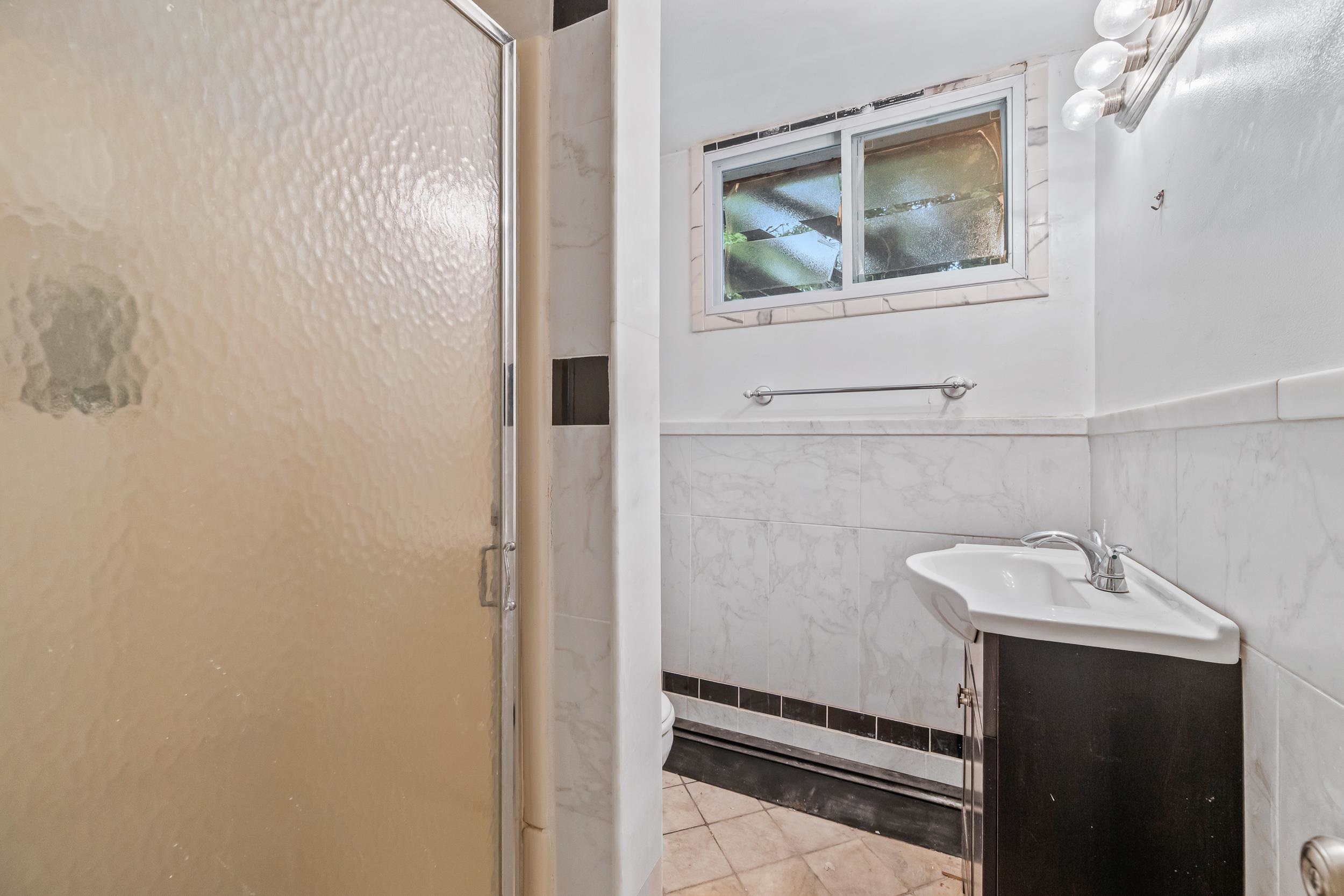 Bathroom with a frosted-glass shower, dark vanity, white sink, and marble-pattern tile.