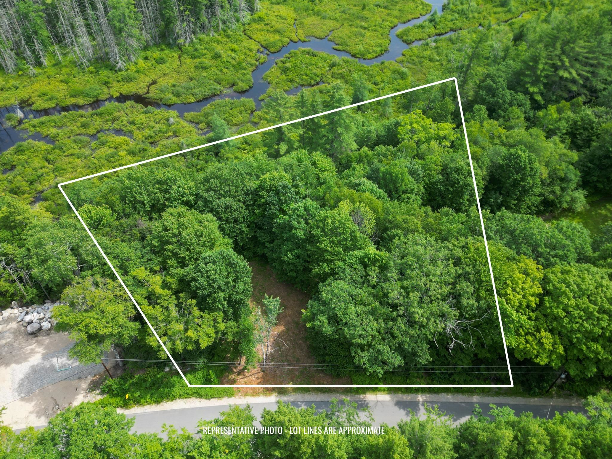 Aerial view of a wooded lot outlined beside a road, with wetlands and winding water nearby.