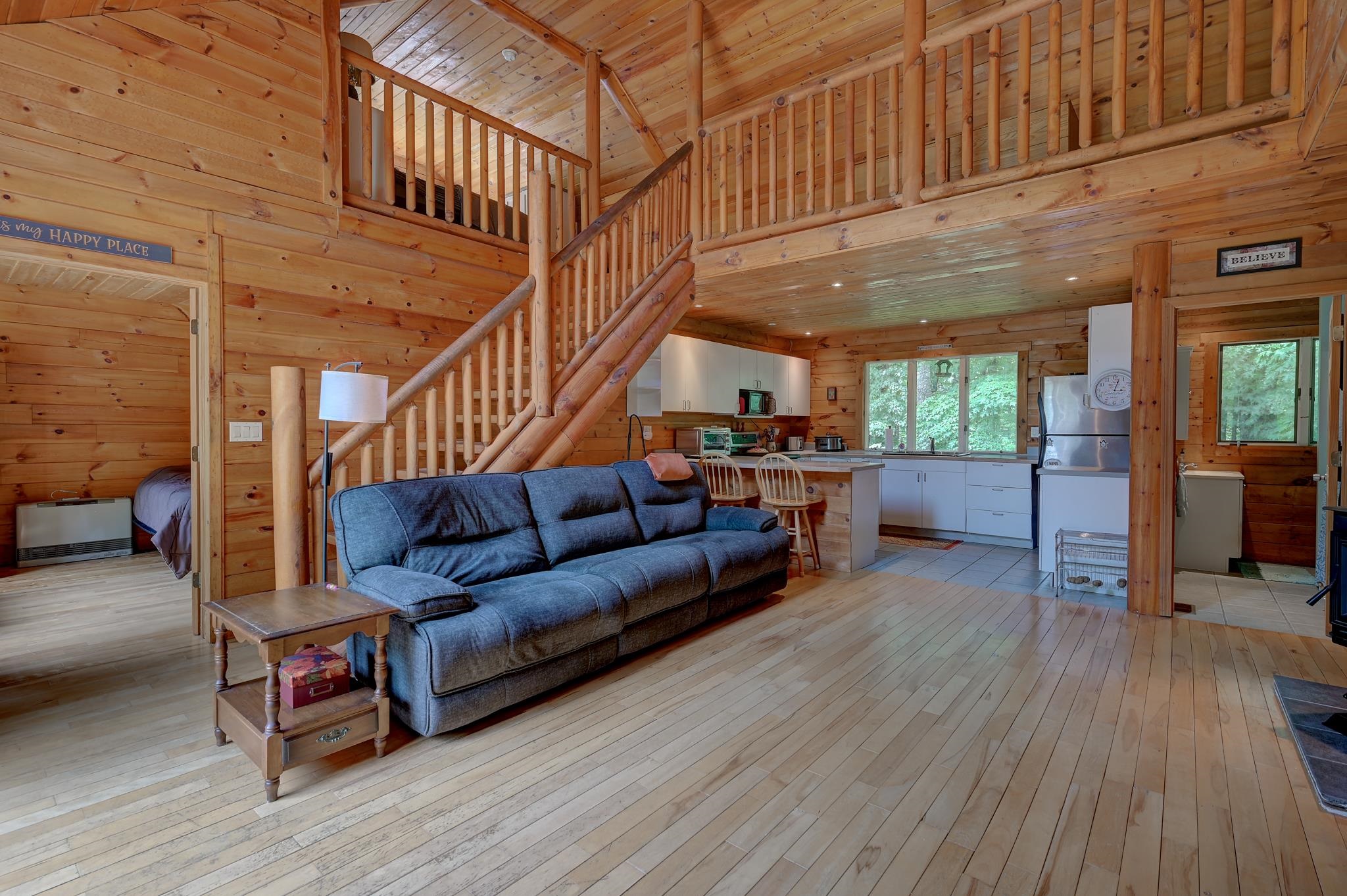 Cabin living room with blue sofa, open staircase, loft, and white kitchen overlooking trees.